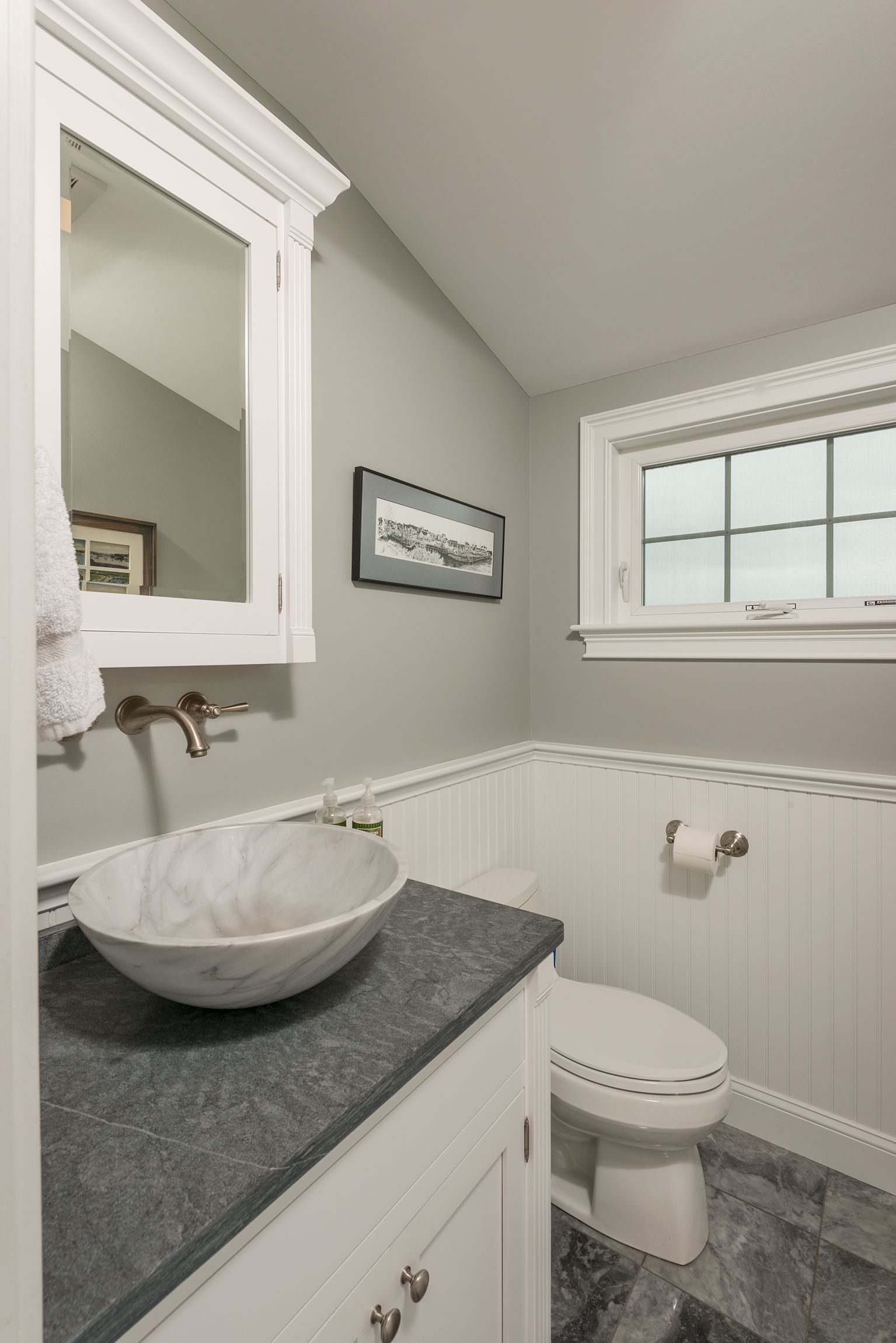 Small white bathroom with vessel sink, gray countertop, toilet, and window.