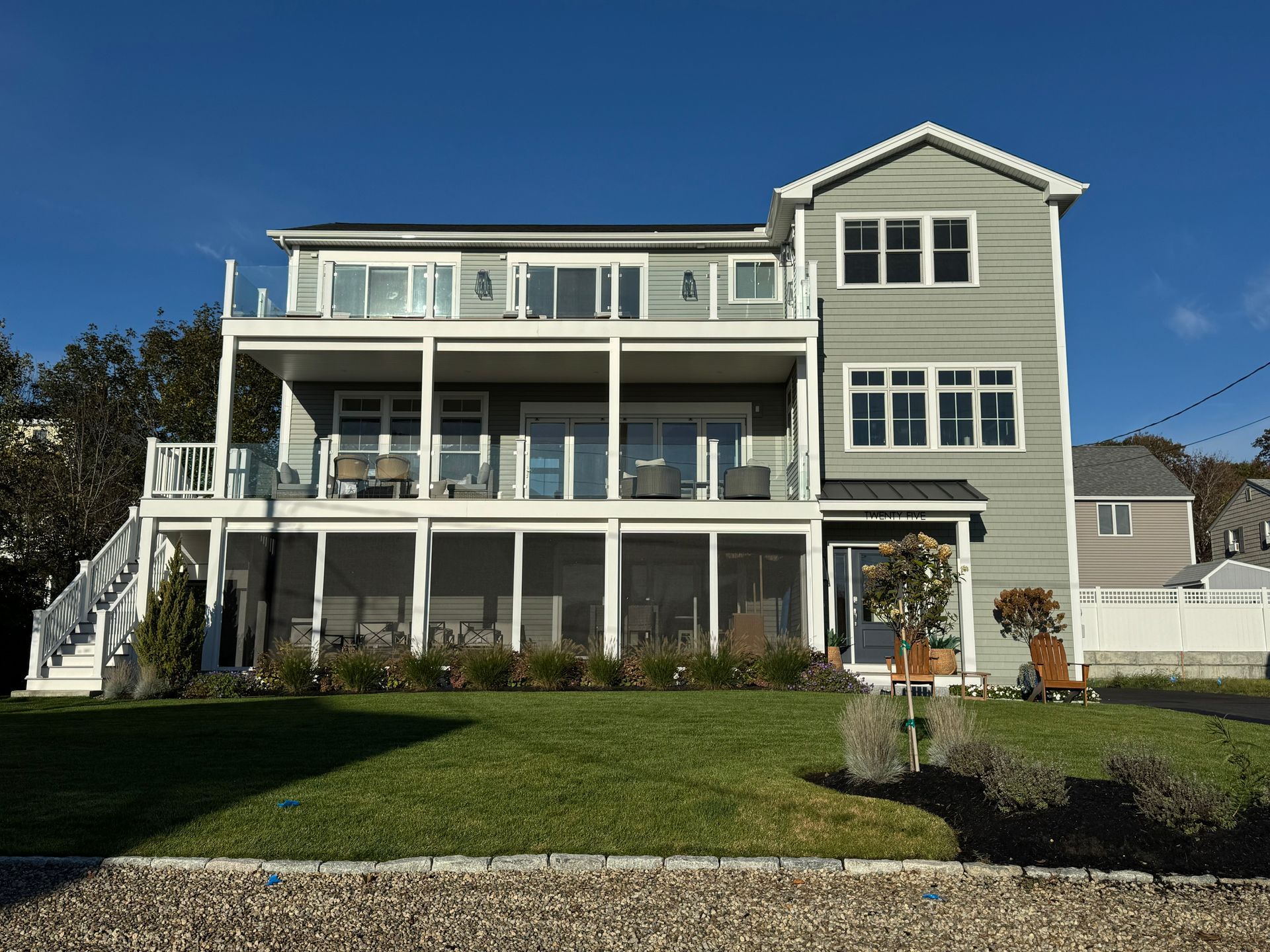 Large gray two-story house with white trim, front porches, and a manicured lawn under a blue sky