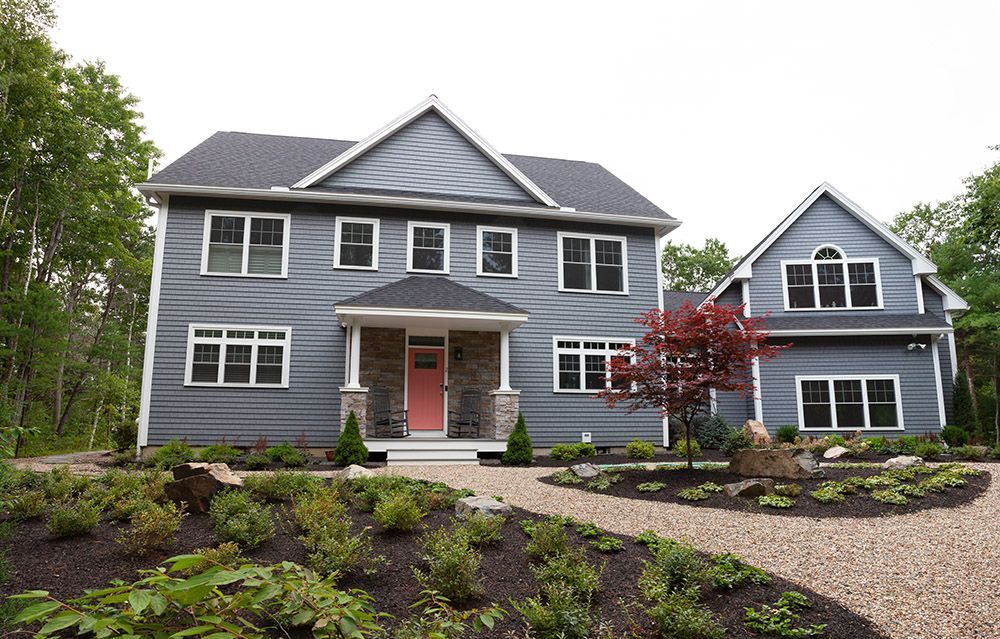 Gray two-story house with white trim, red front door, and landscaped yard under overcast skies