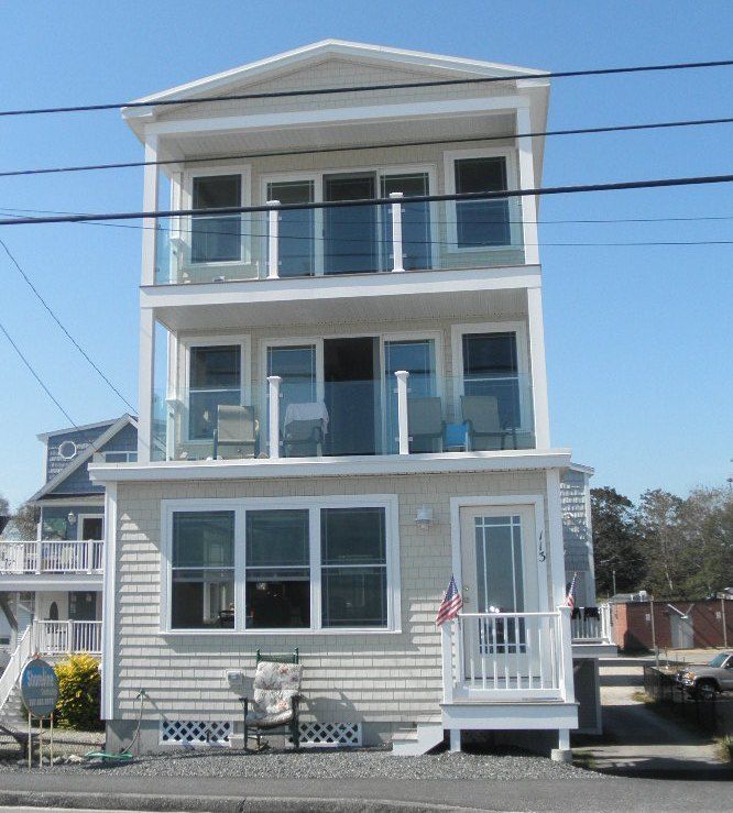 Three-story white beach house with blue shutters and front porch under a clear sky