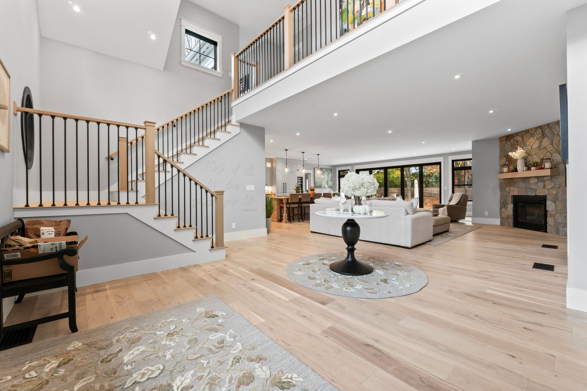 Bright modern open-plan living room with white sofas, wood floors, staircase, and large windows
