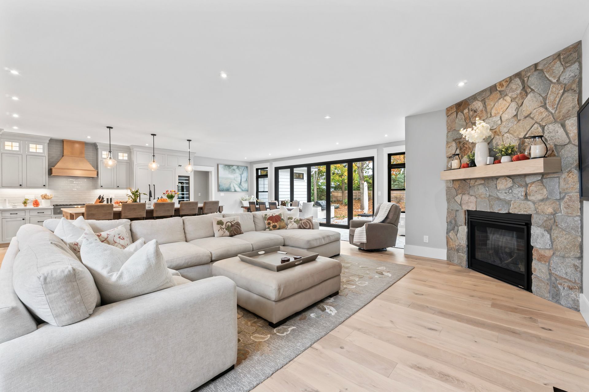 Bright modern living room with beige sectional, stone fireplace, and open kitchen