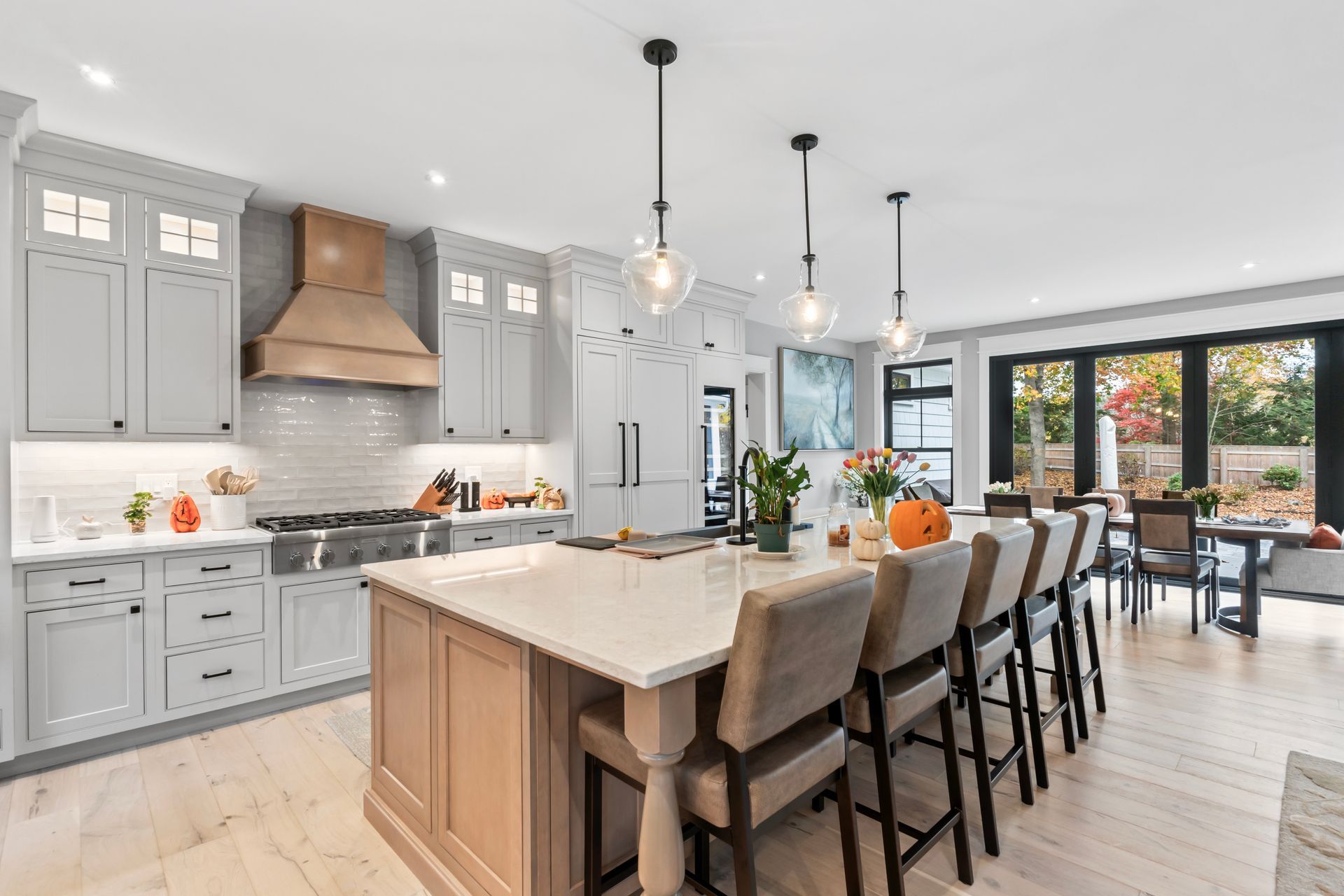 Bright modern kitchen with gray cabinets, wood island, black barstools, and large windows opening to a patio