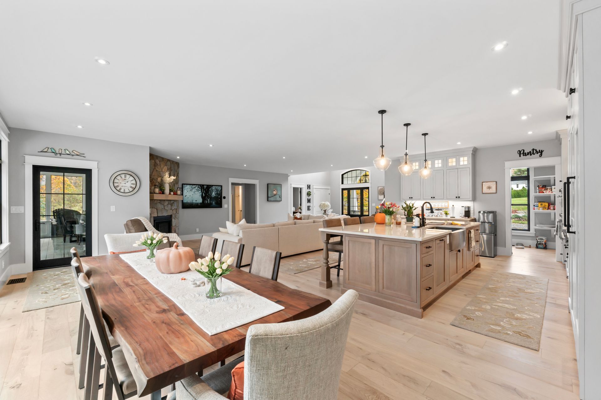 Open-concept kitchen and dining room with light wood floors, gray cabinets, and a long wooden table.