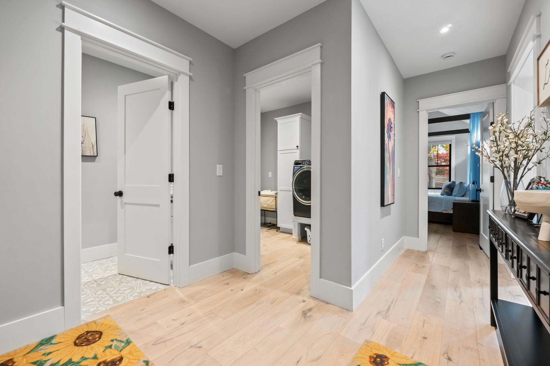 Bright hallway with gray walls, white doors, and light wood floors leading to a bedroom and bathroom.