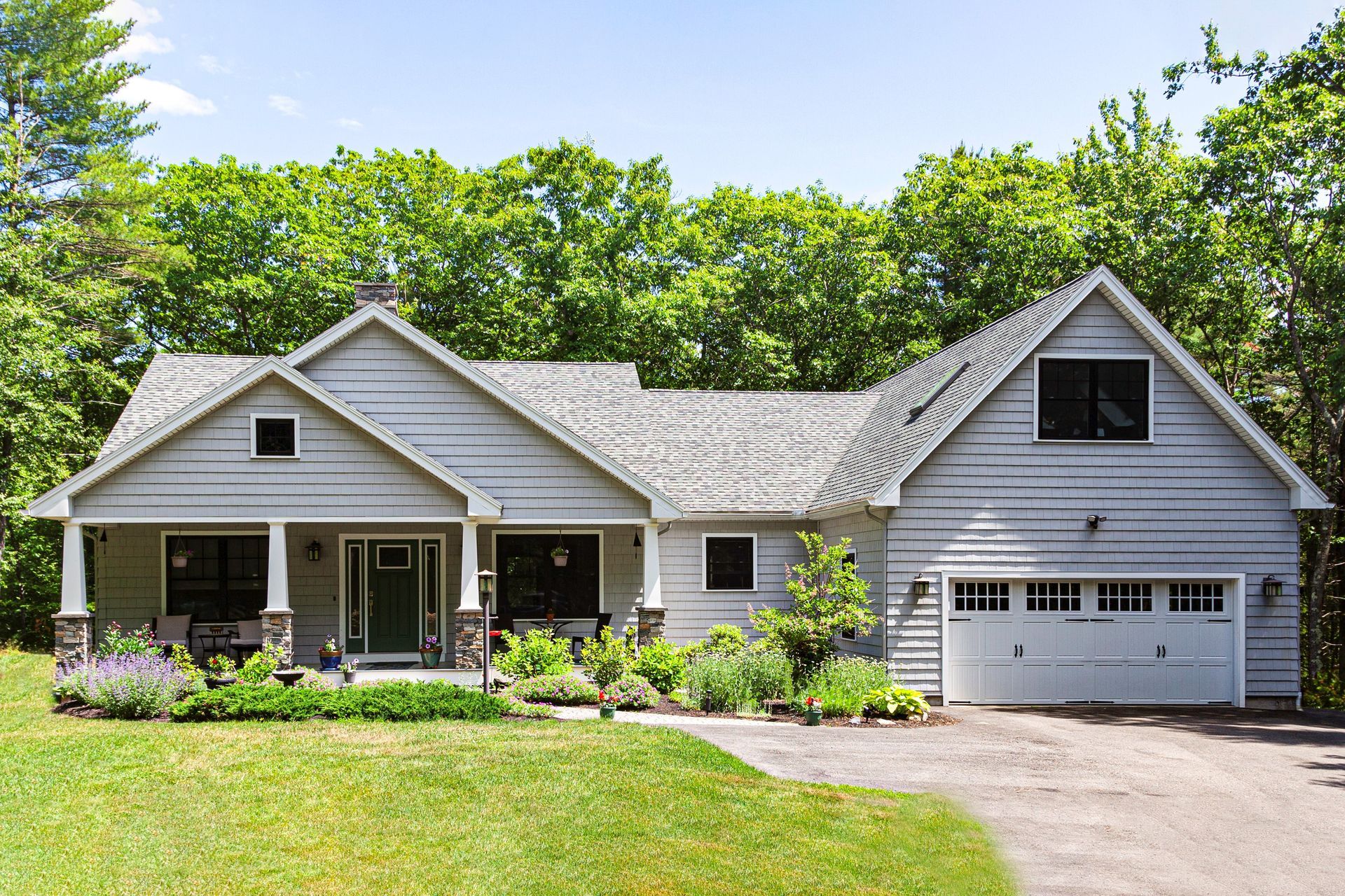 Single-story white house with gray roof, front porch, garage, and green lawn under a sunny sky