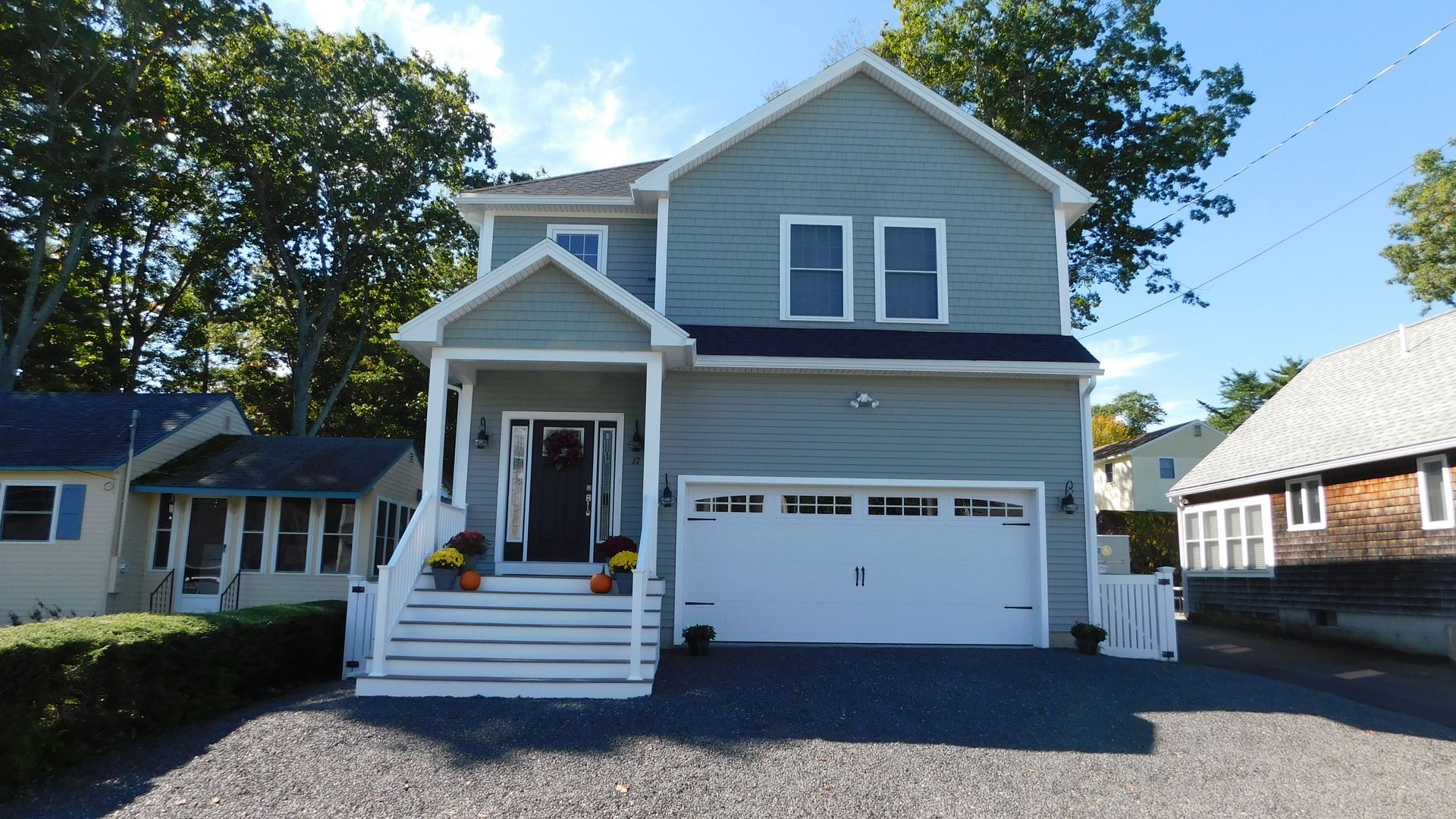 Two-story gray house with white trim, front porch, and attached garage on a sunny day