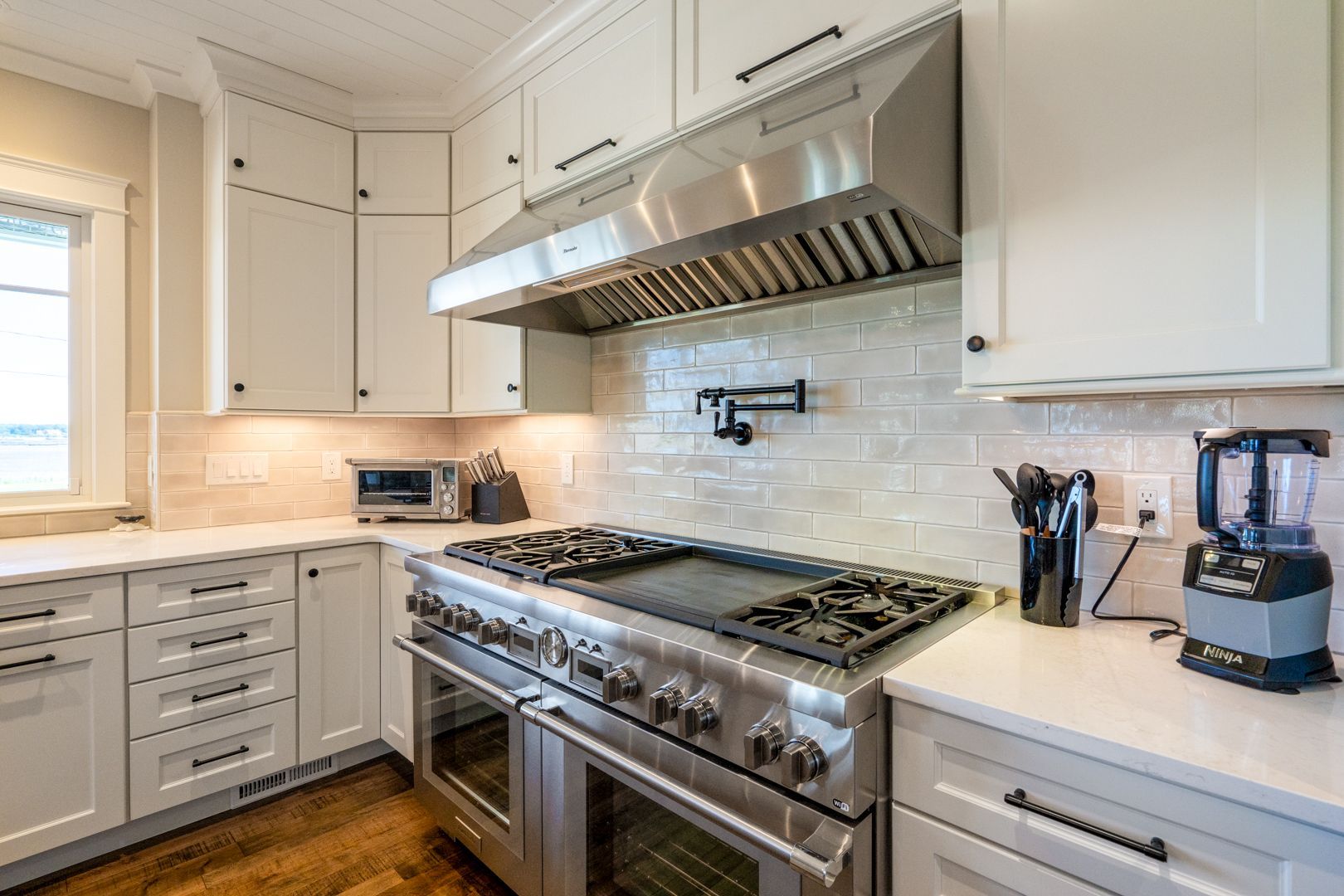 Bright white modern kitchen with stainless steel range, tiled backsplash, and countertop blender