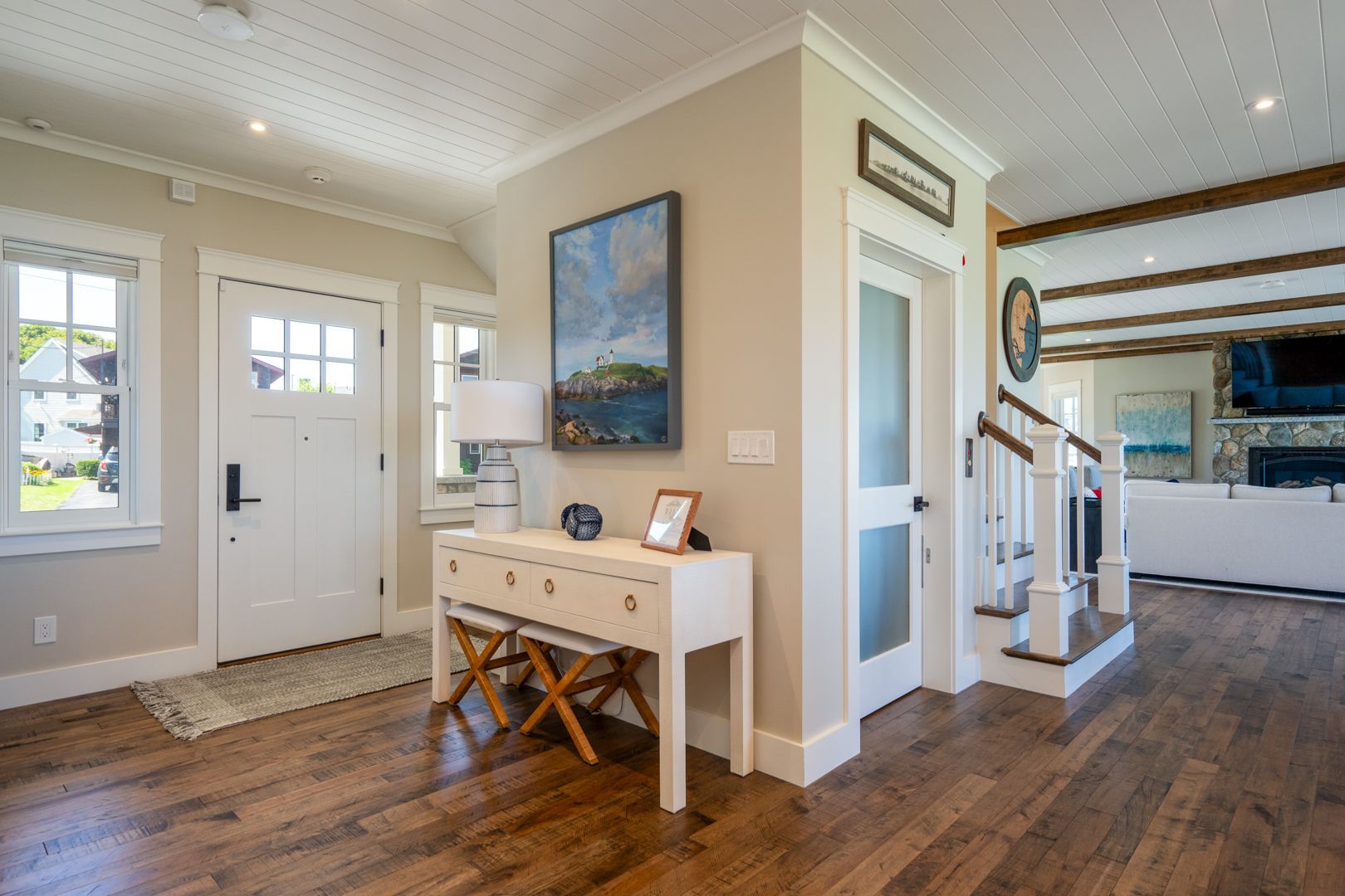 Bright entryway with white front door, console table, stairs, and hardwood floors in a modern home