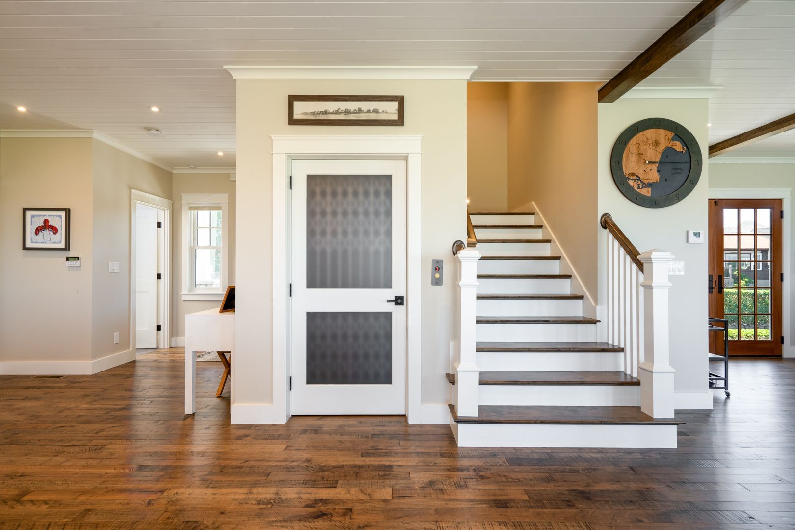 Bright foyer with hardwood floors, white staircase, and elevator-style door in a modern home