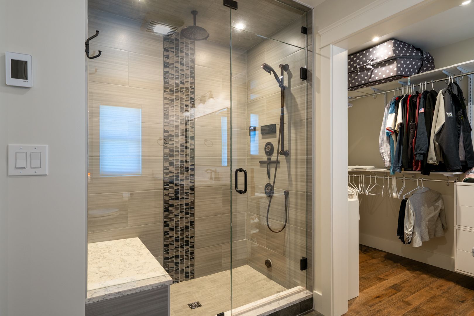 Walk-in shower with glass door and mosaic tile, beside an open closet with hanging clothes