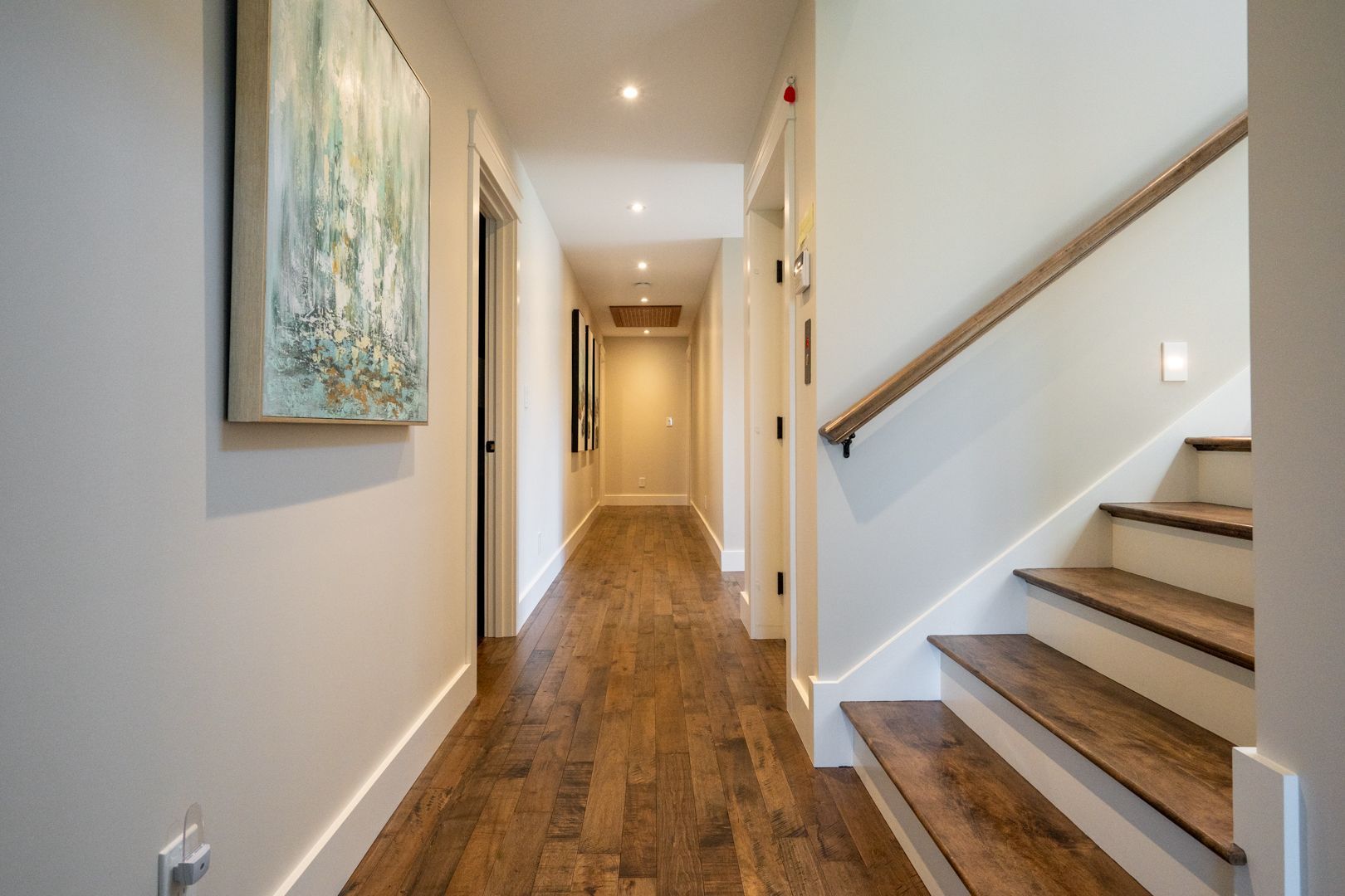 Bright hallway with wood floors, beige walls, wall art, and stairs on the right
