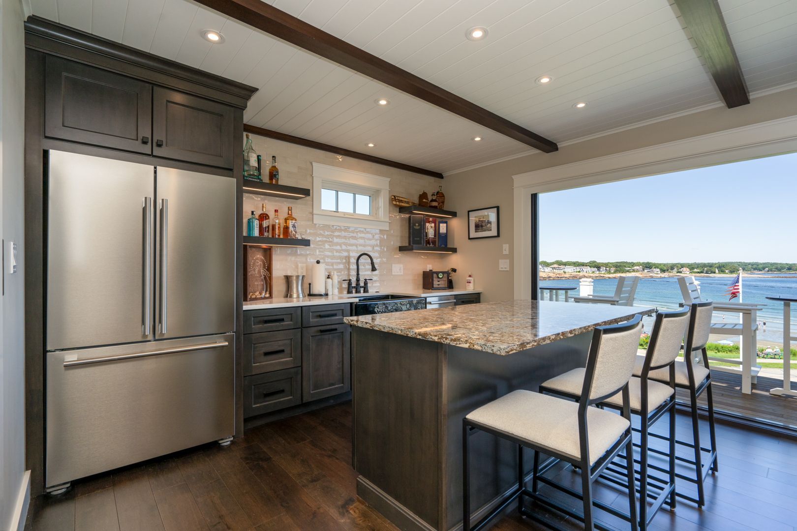 Modern kitchen with stainless appliances, granite island, and bar stools overlooking a waterfront view