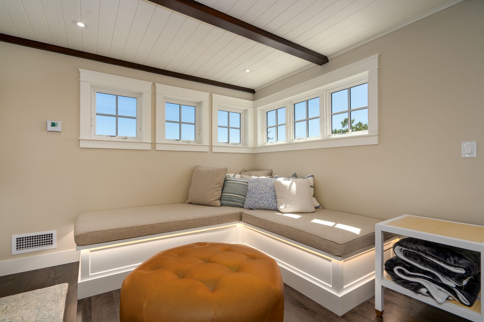 Cozy window nook with built-in bench, beige cushions, and an orange ottoman in a bright room