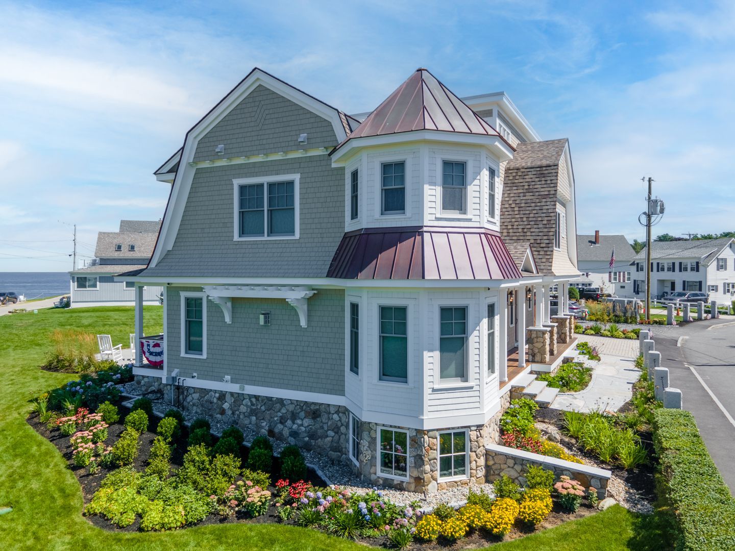 Coastal gray house with red metal roof, white trim, and landscaped garden beside the street