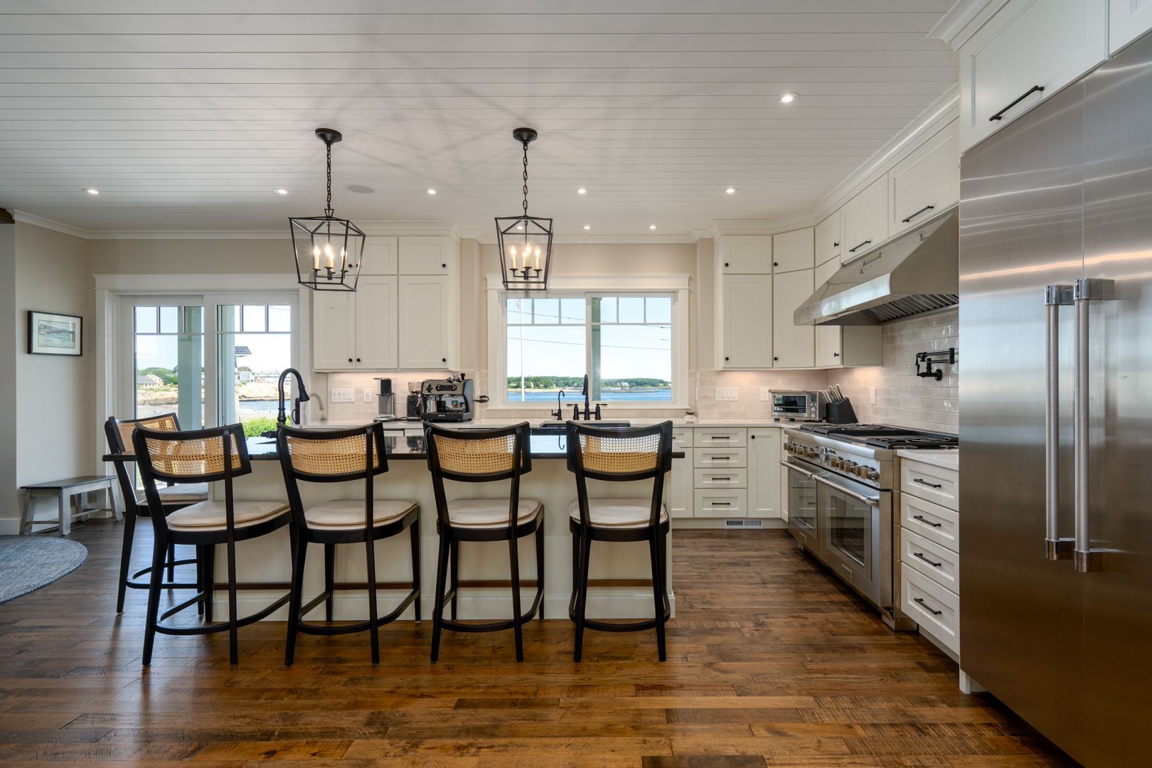 Bright modern kitchen with white cabinets, wood floors, island seating, stainless appliances, and pendant lights