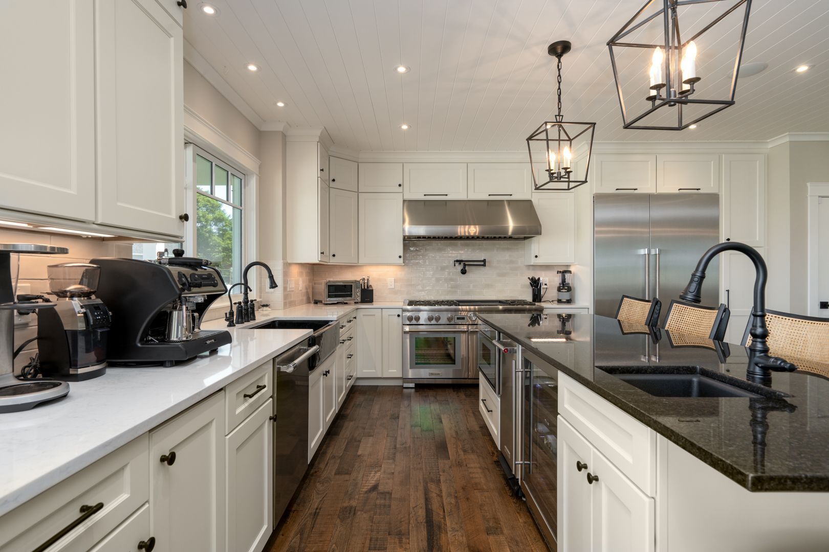 Modern white kitchen with black countertops, island sink, stainless appliances, and pendant lights