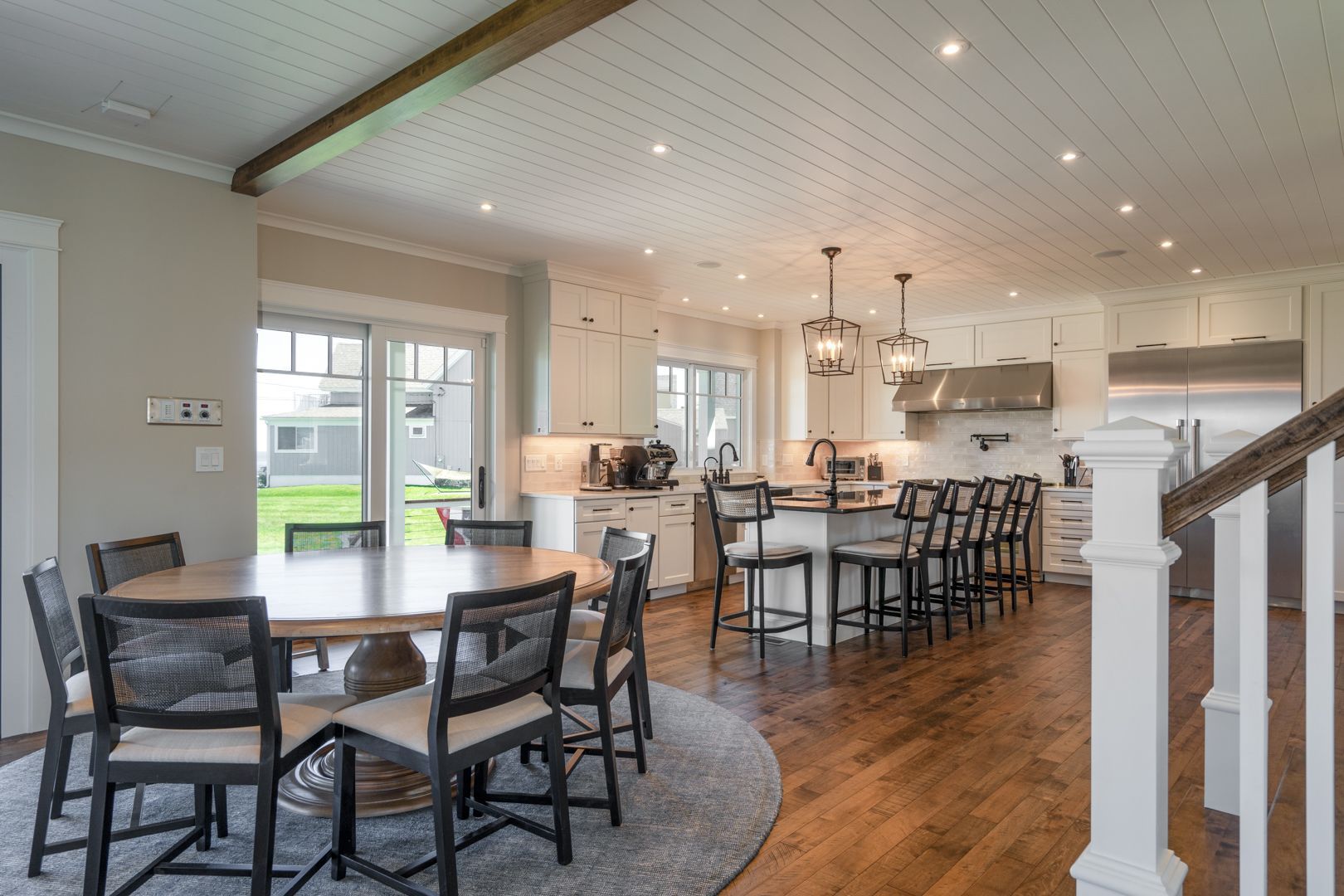 Open-concept dining and kitchen area with wood floors, round tables, and bar stools