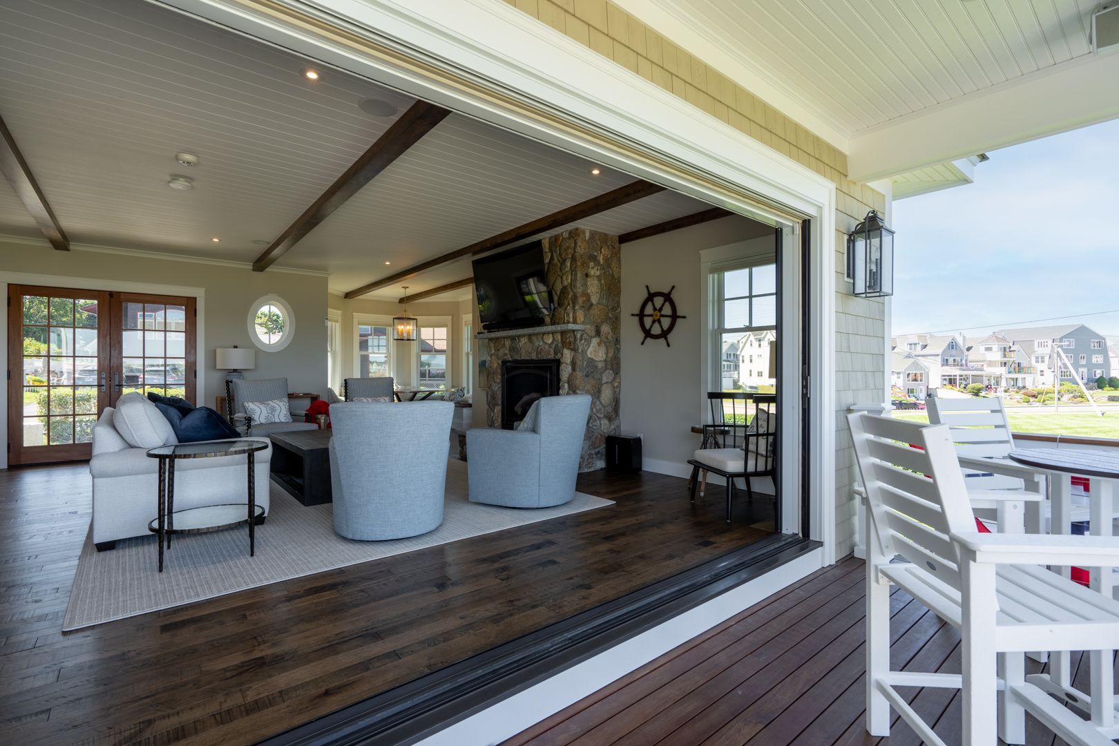 Covered patio with gray chairs, wood floor, and open view to a waterfront deck