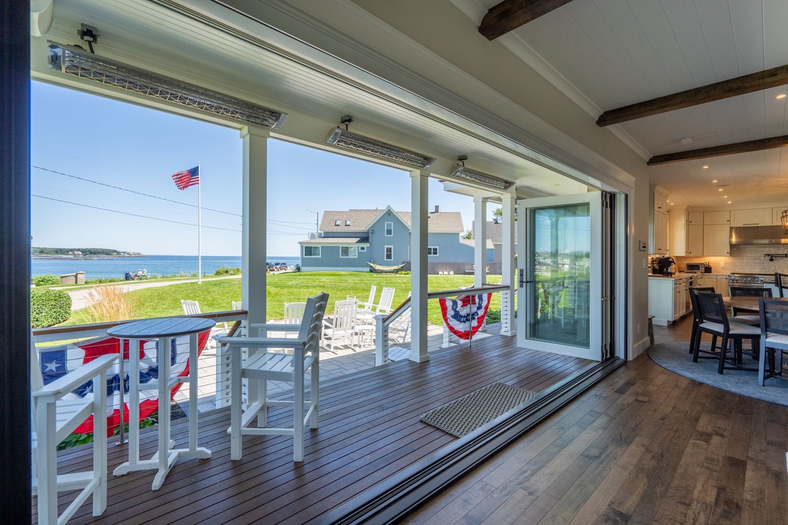 Bright beach house deck with sliding glass doors, white chairs, and ocean view