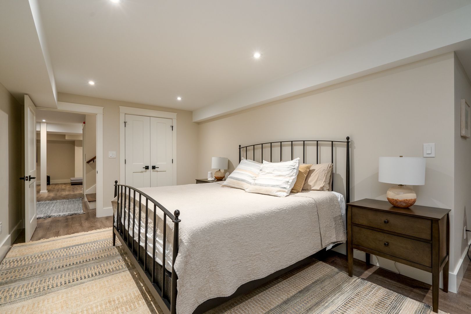 Bright bedroom with metal bed frame, striped rug, and wood nightstand with lamp