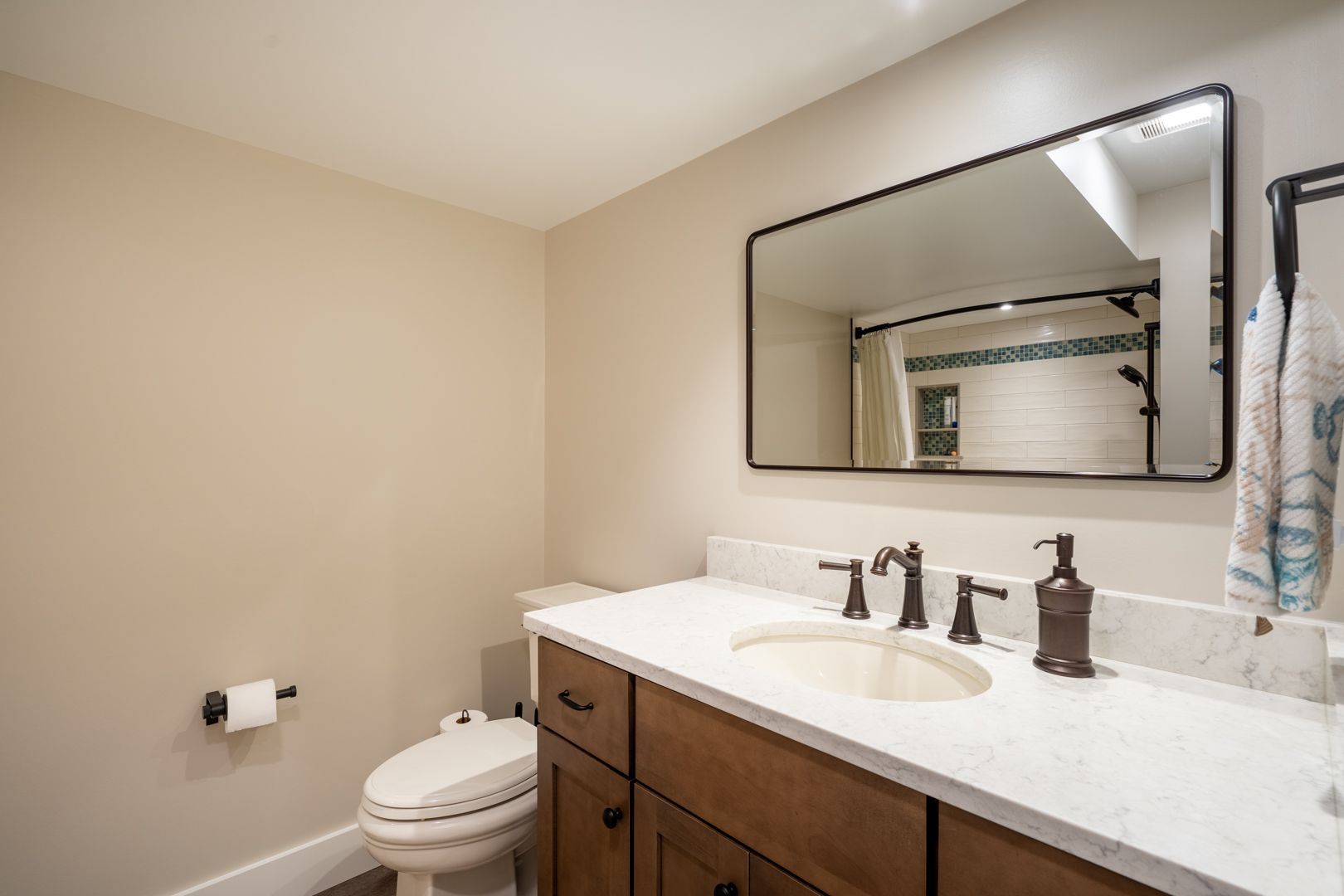 Bathroom vanity with white countertop, wooden cabinets, toilet, and large mirror against beige walls
