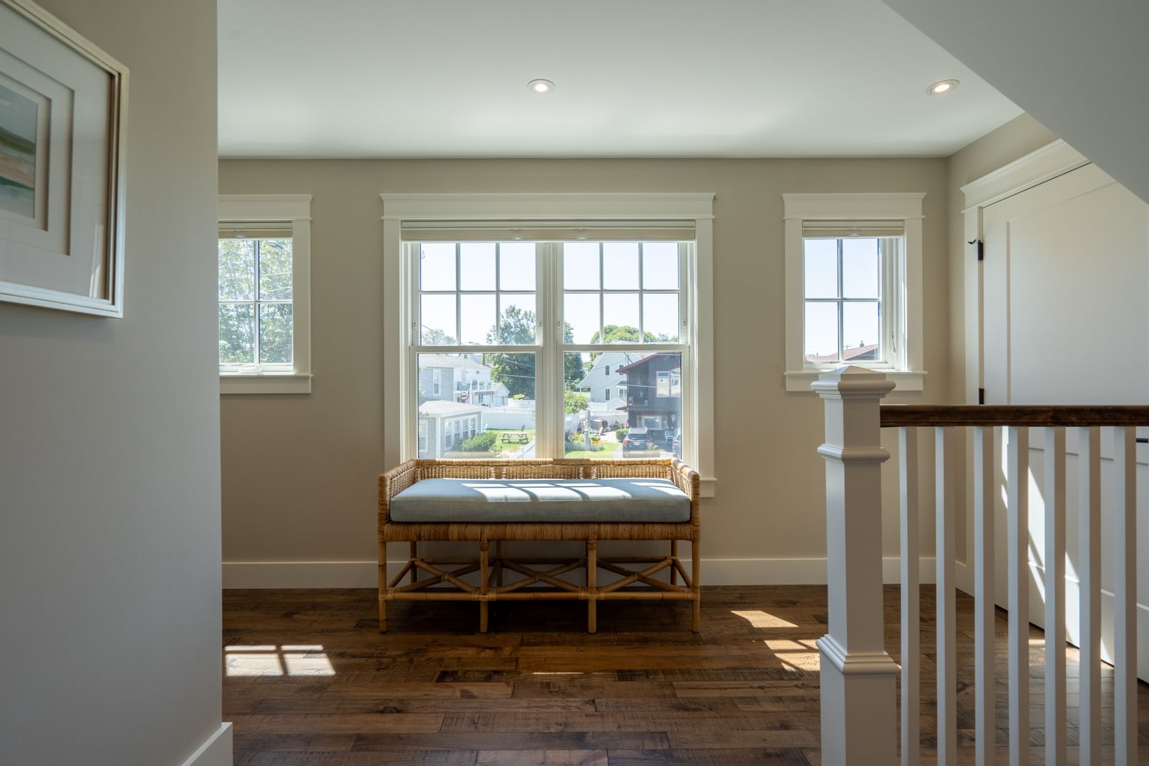 Bright upstairs landing with a cushioned bench by two windows and a staircase railing on the right