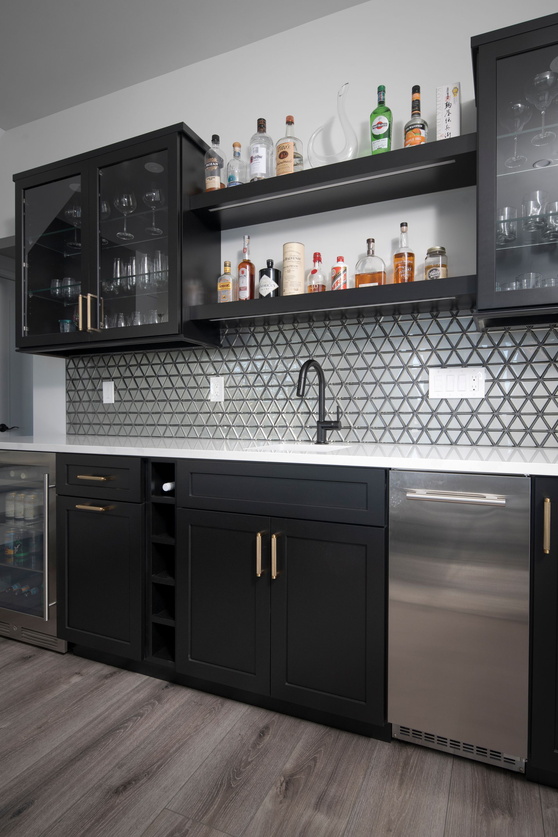 Modern black kitchen bar with glass cabinets, herringbone tile backsplash, and stainless steel dishwasher