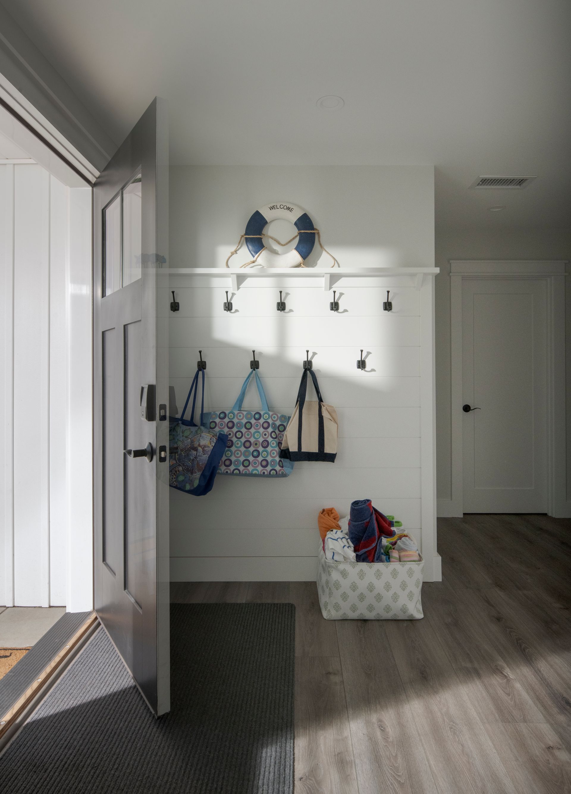Bright entryway with hooks, tote bags, a storage bench, and two bird figures on a shelf by a sunlit door