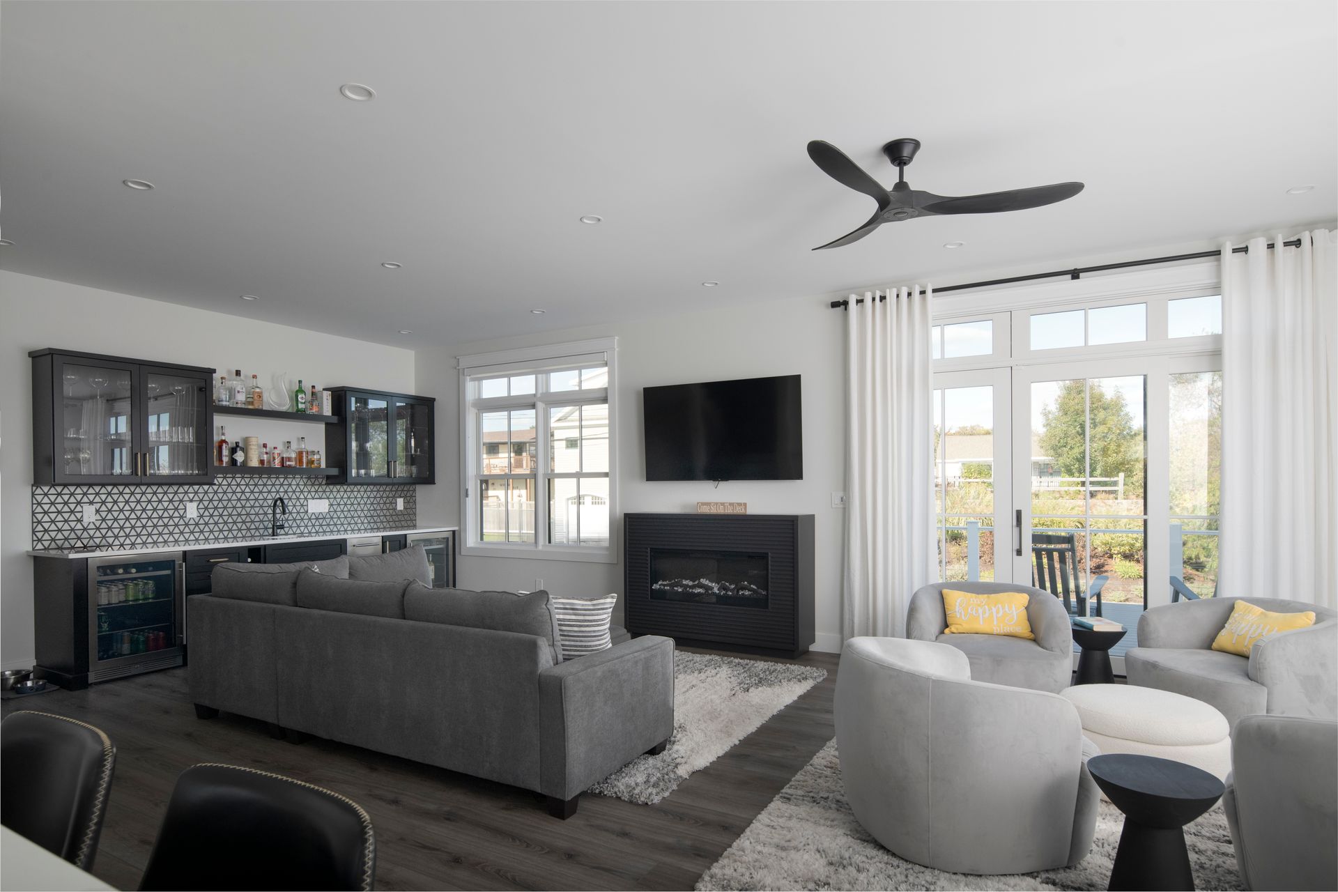 Modern living room with gray sectional, fireplace, wall TV, and large windows overlooking a balcony.