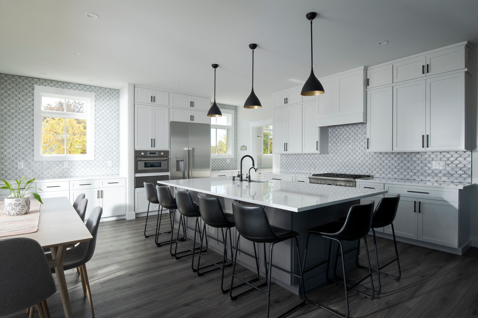 Modern white kitchen with large island, black barstools, pendant lights, and dark wood floors