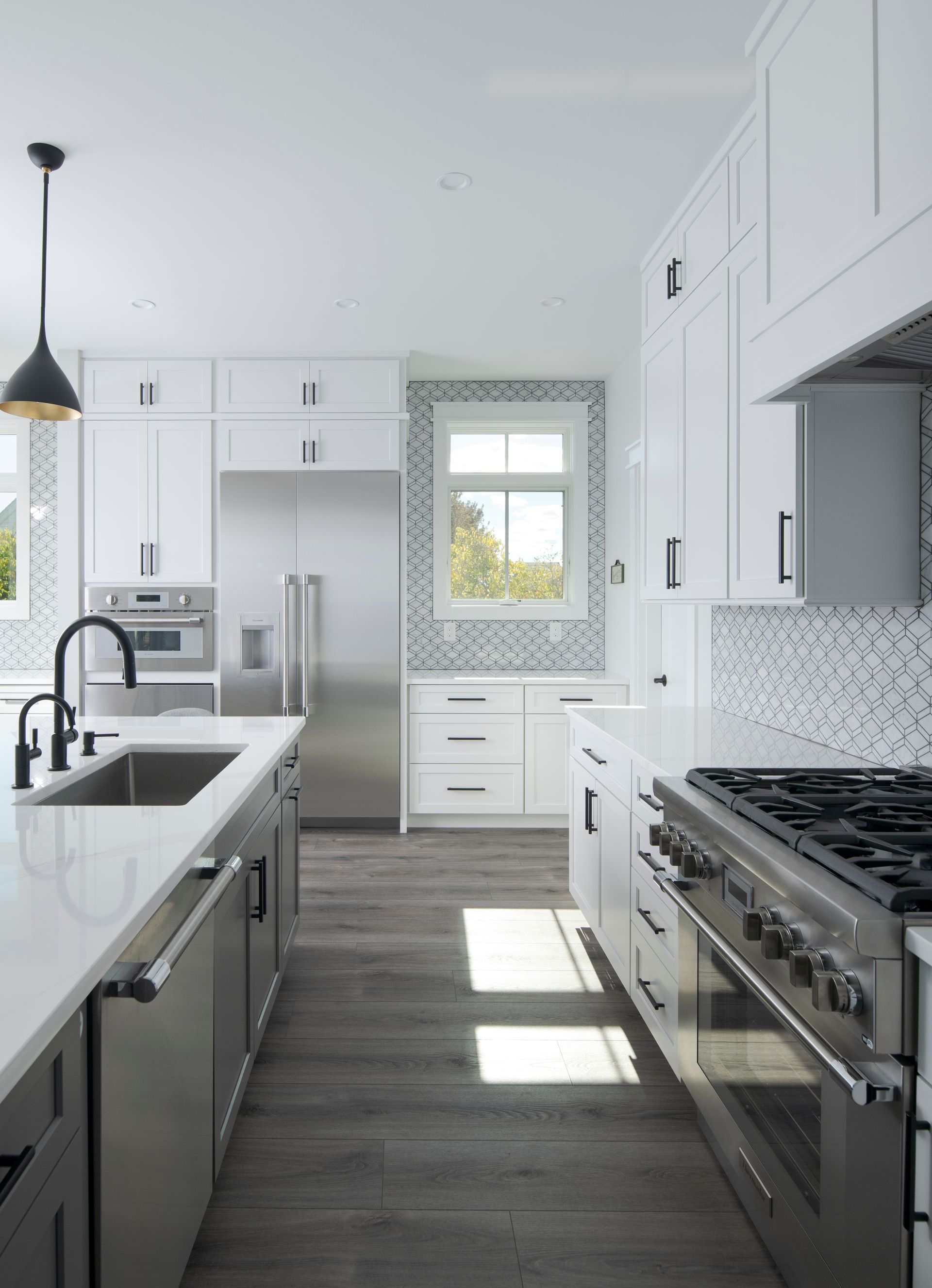 Bright white kitchen with gray island, stainless stove, pendant lights, and sunlit window.