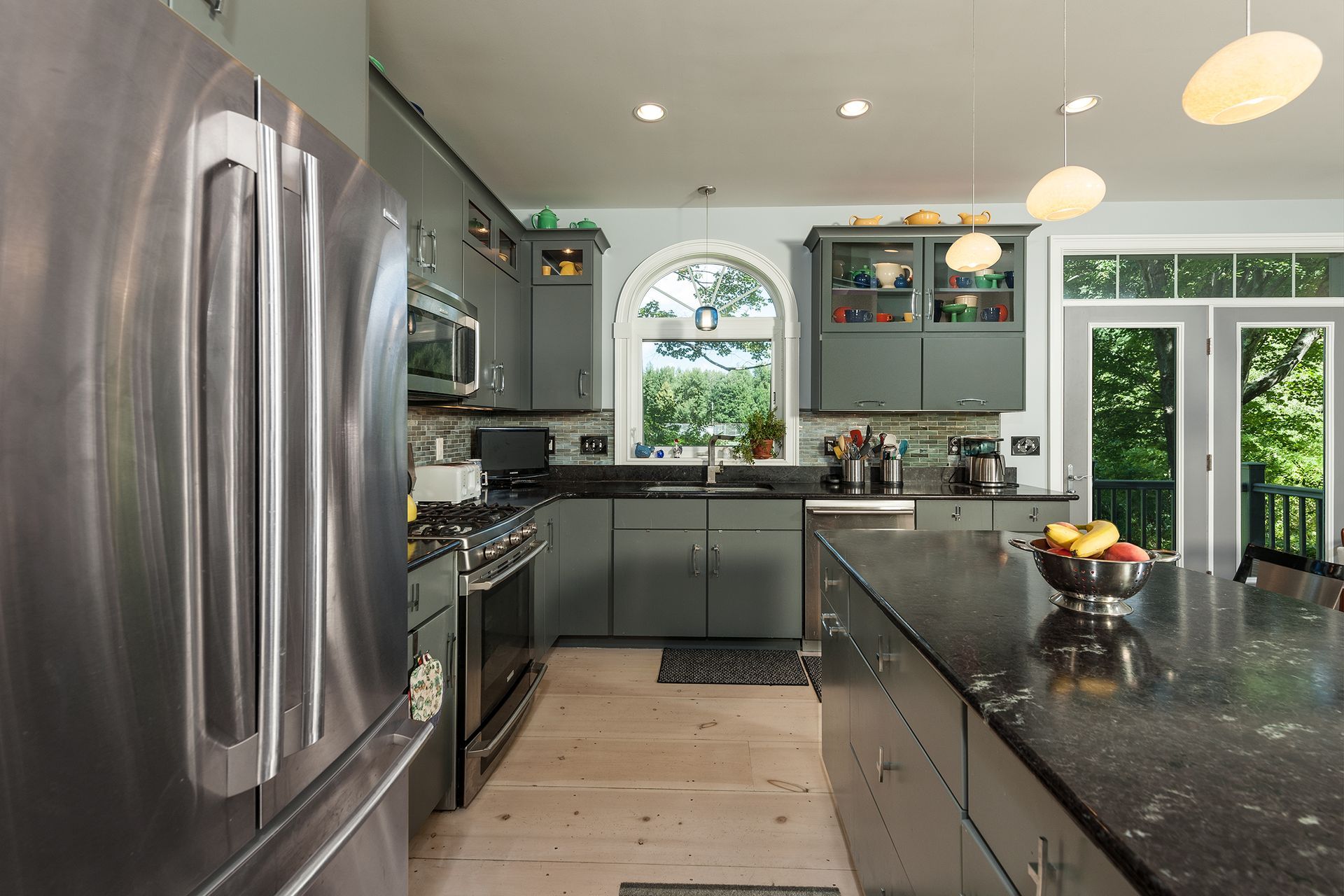 Modern kitchen with stainless steel fridge, island, gray cabinets, and large window overlooking greenery