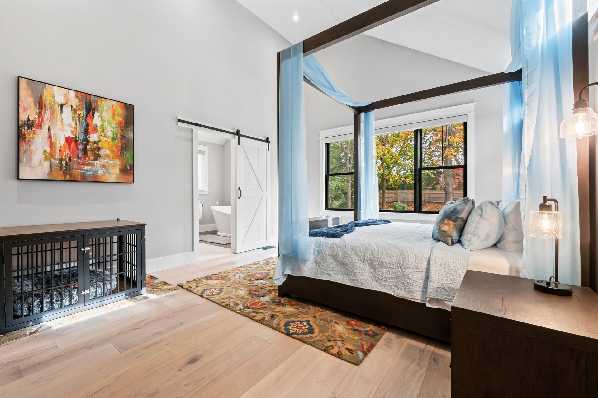 Bright modern bedroom with canopy bed, large windows, patterned rug, and wall art