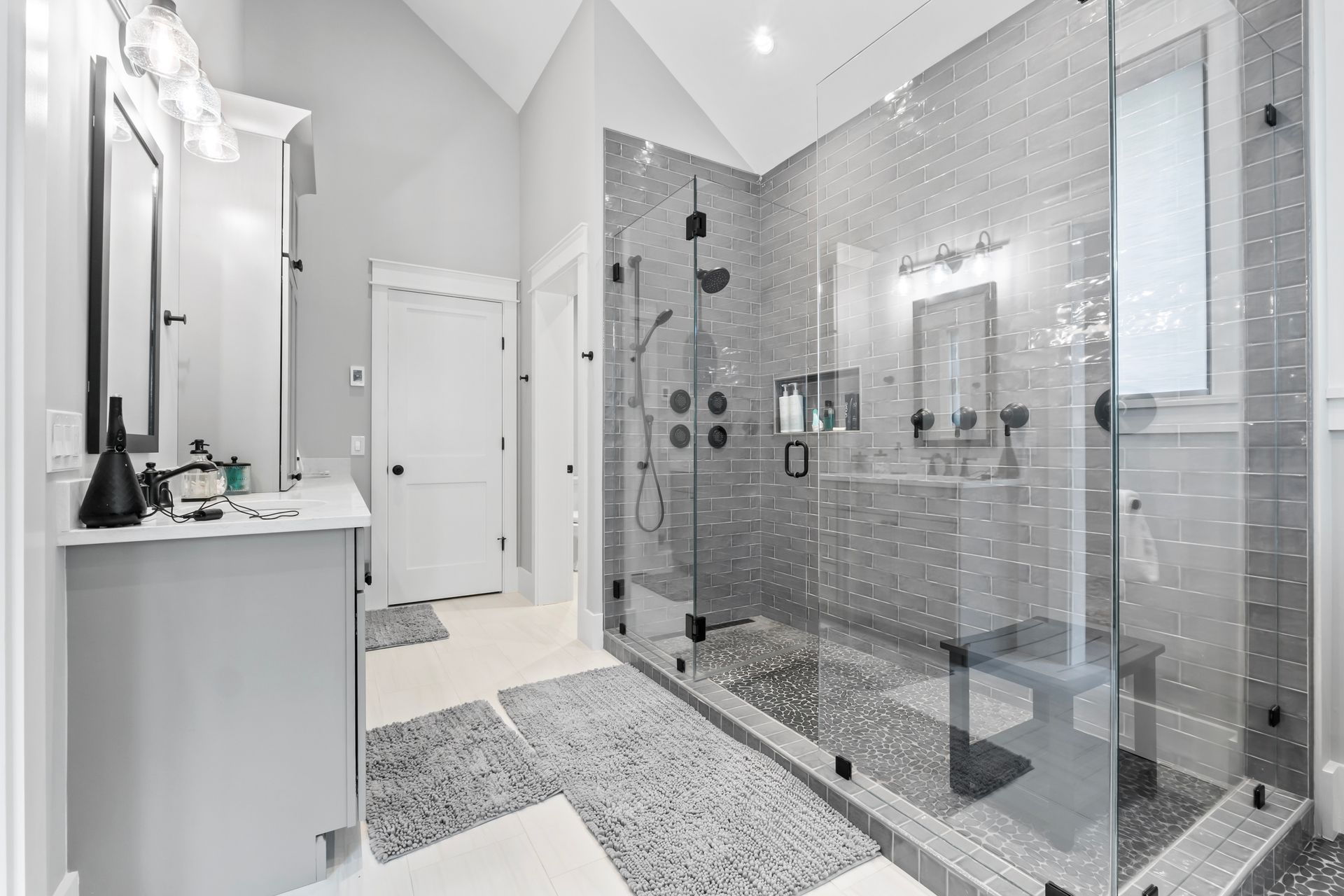 Bright modern bathroom with glass shower, white vanity, and gray tile floor