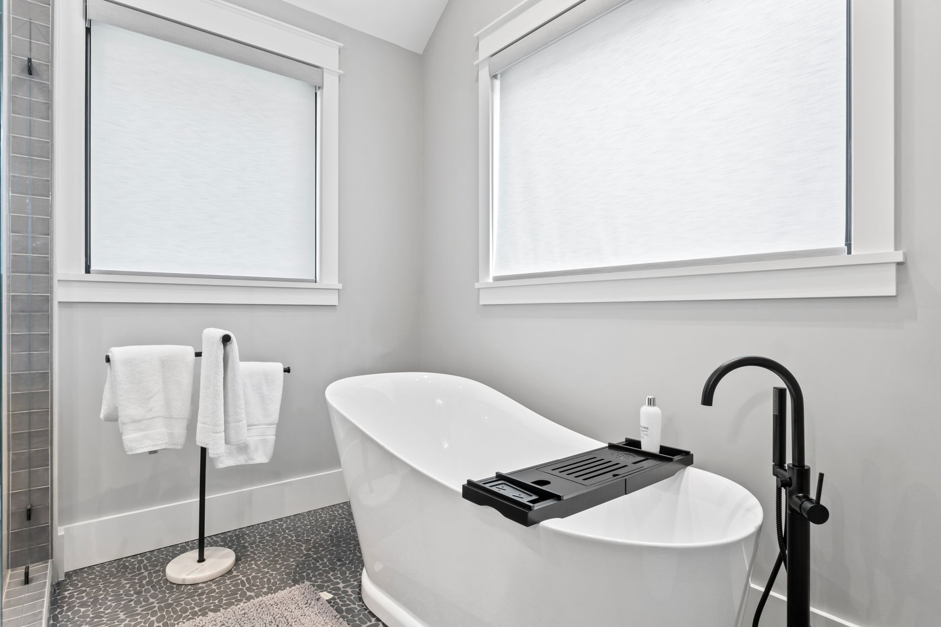 Modern bathroom with a white soaking tub, black floor faucet, towel rack, and gray walls
