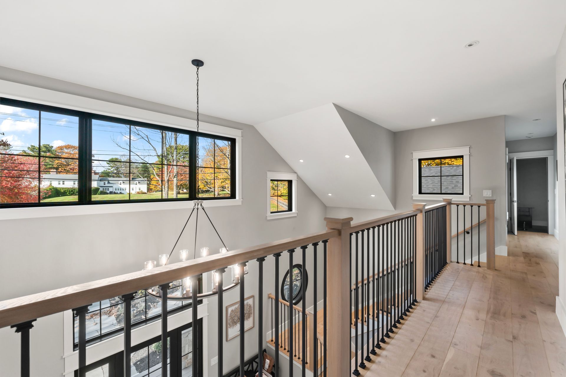 Modern bright hallway with black railing, light wood floors, and large windows overlooking trees