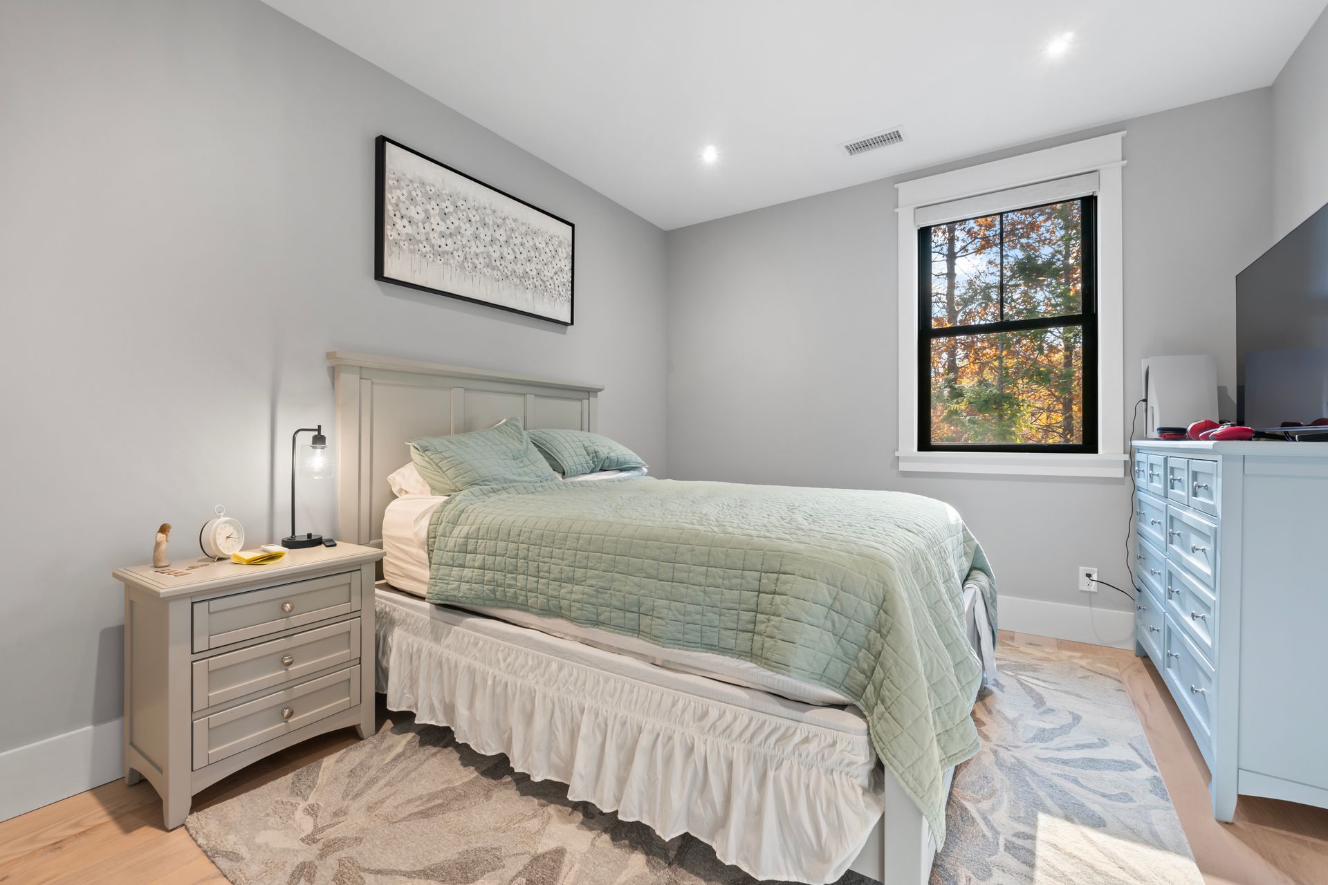 Bright bedroom with a bed, nightstand, blue dresser, and a window with daylight.