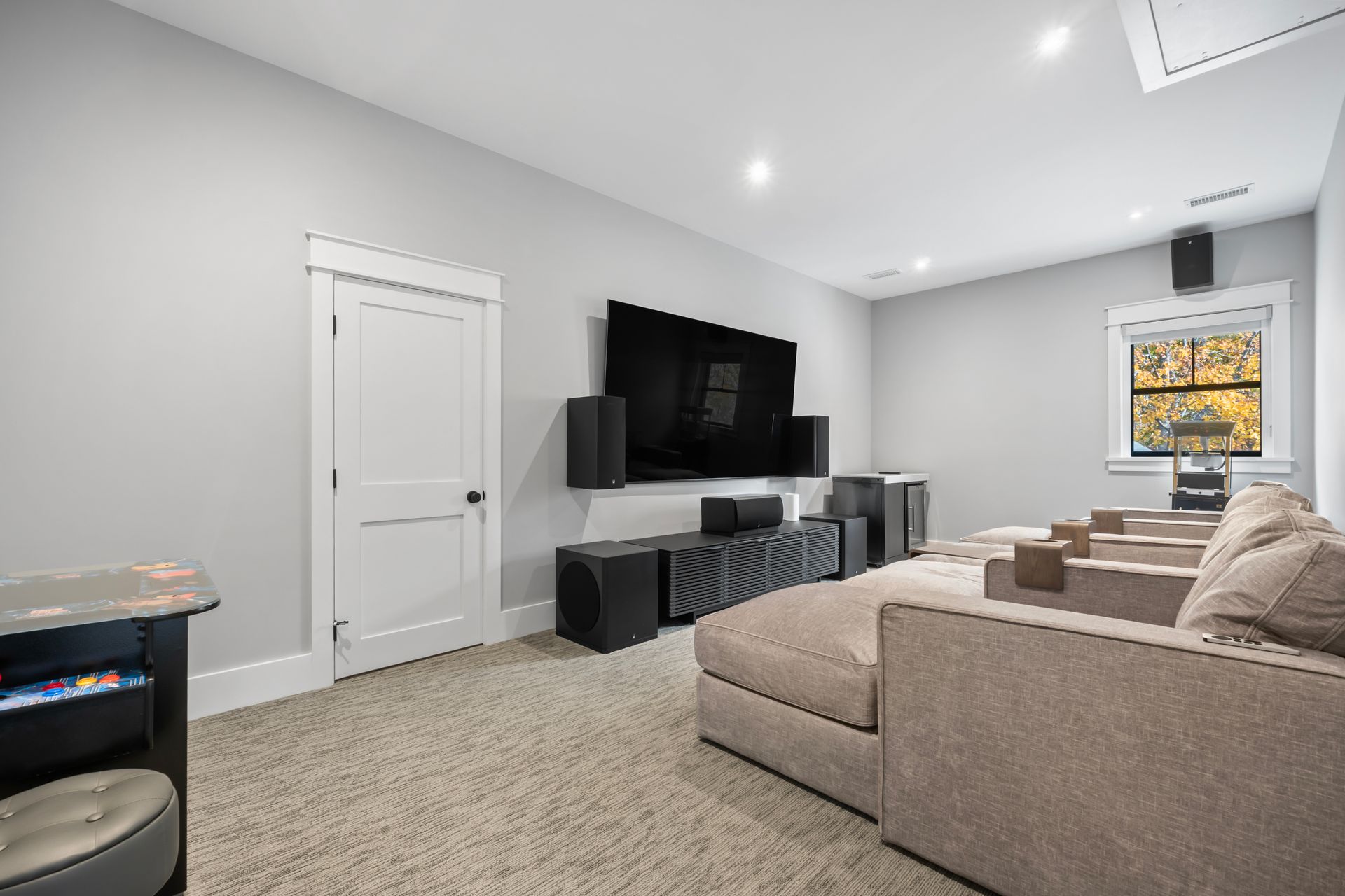 Bright modern living room with beige sectional sofa, wall-mounted TV, black consoles, and carpeted floor