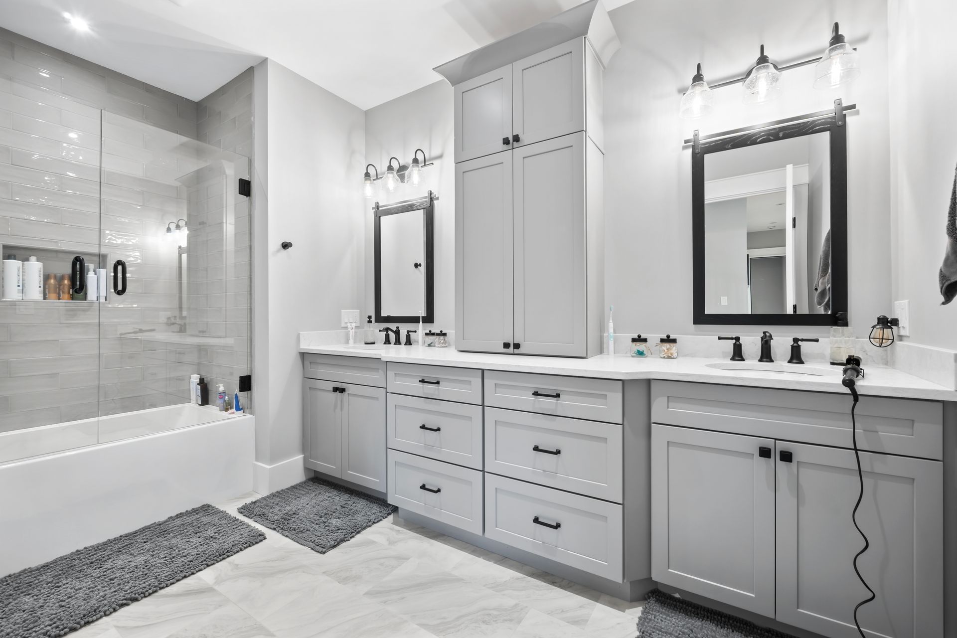 Bright modern bathroom with double vanity, large mirrors, and bathtub with gray tile accents
