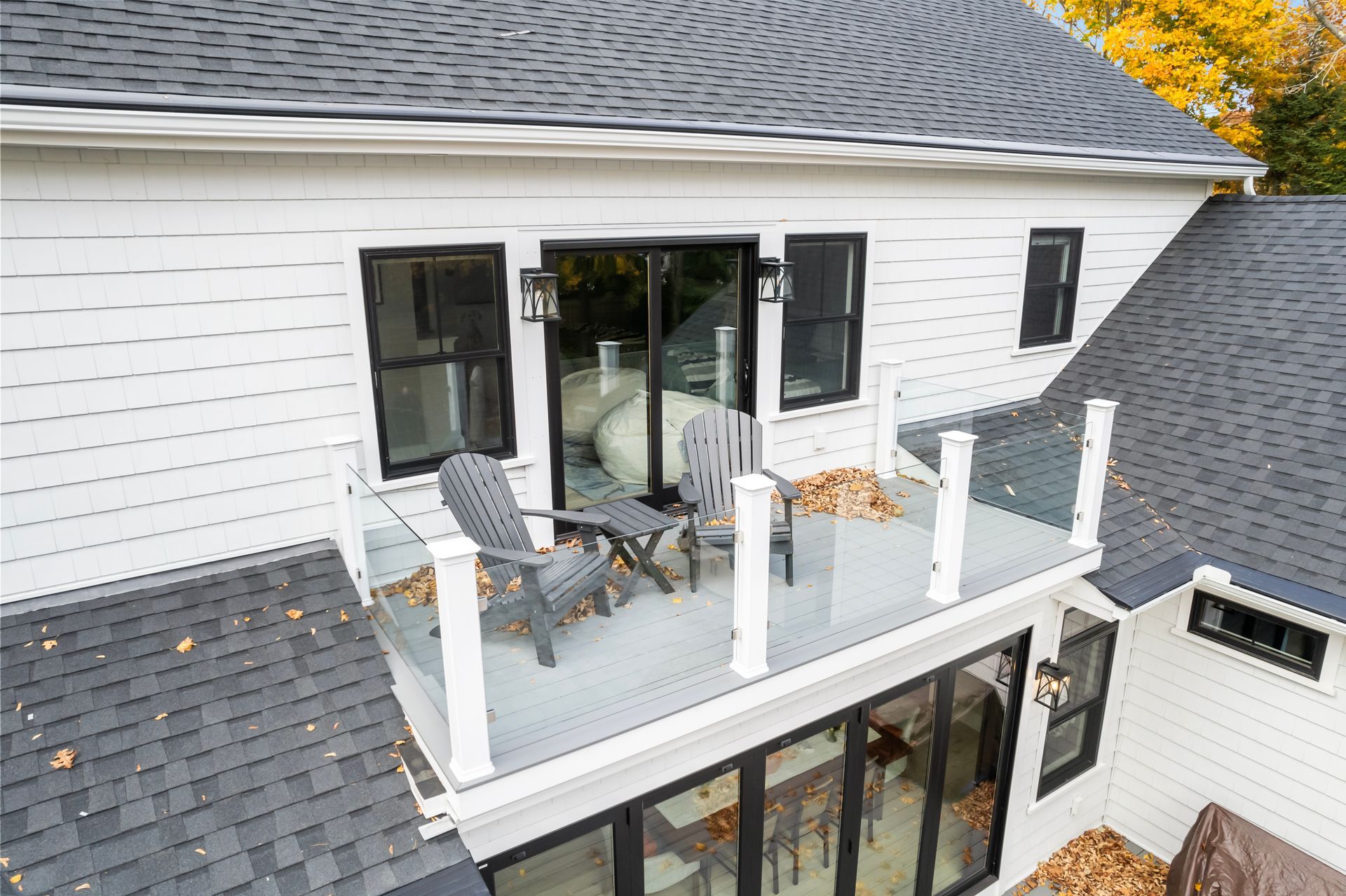 Second-story balcony with glass railing, patio chairs, and sliding doors on a white house