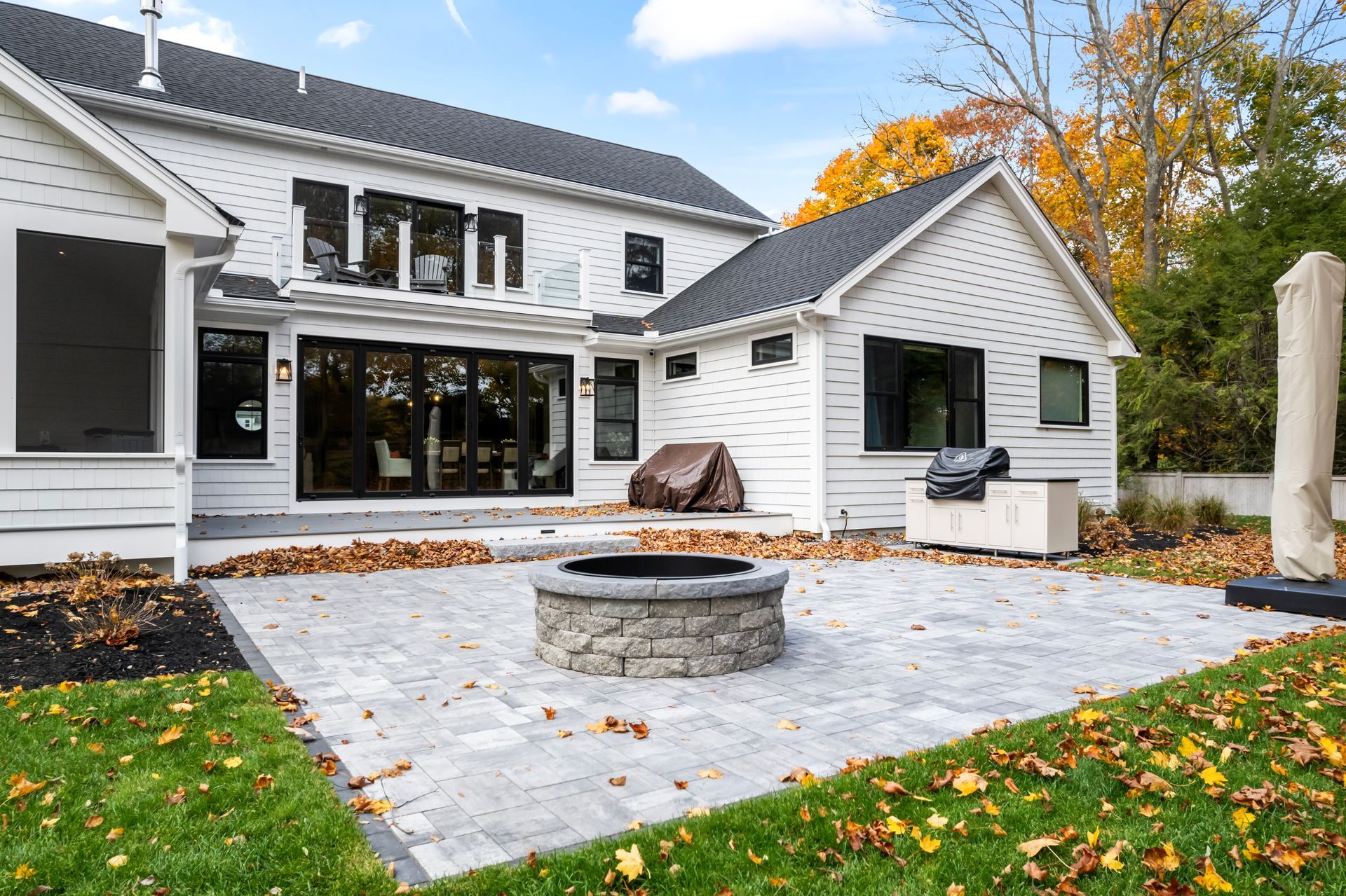 Modern white house with patio, fire pit, and autumn leaves in the backyard