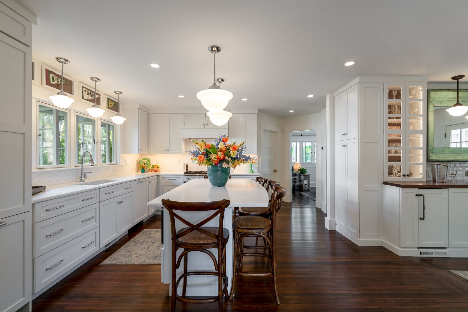 Bright modern kitchen with white cabinets, dark wood floor, island, and colorful flower centerpiece