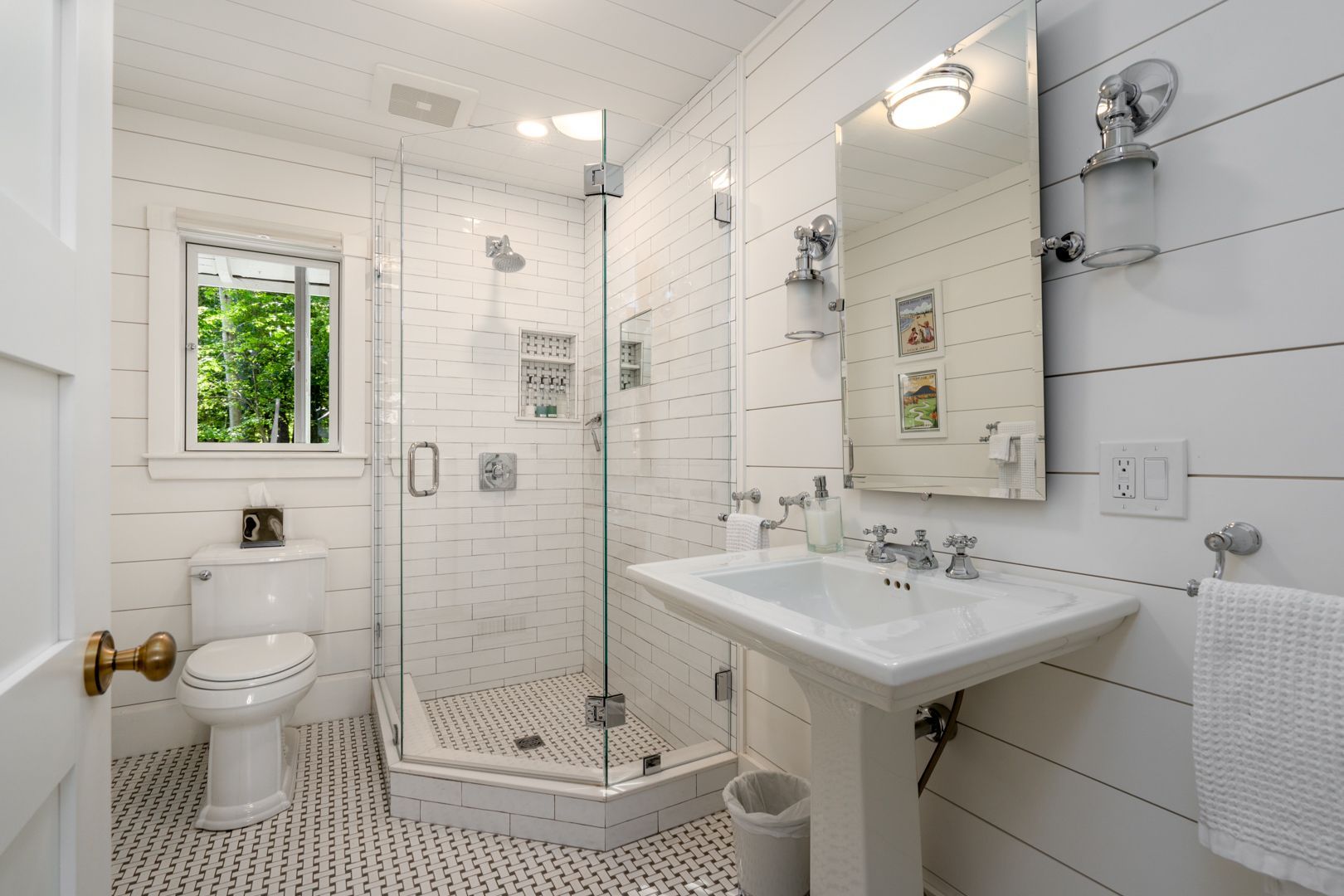 Bright white bathroom with glass shower, pedestal sink, toilet, and tiled floor