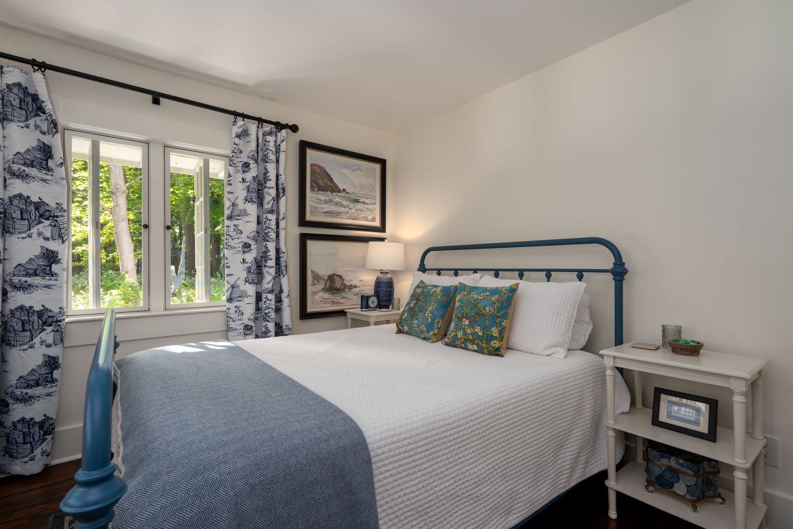 Bright bedroom with blue and white decor, bed by a window, and ocean-themed curtains and accents