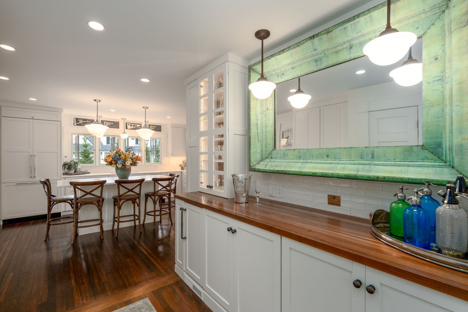 Bright modern kitchen with white cabinets, wood countertops, and a large green-framed mirror over a console.
