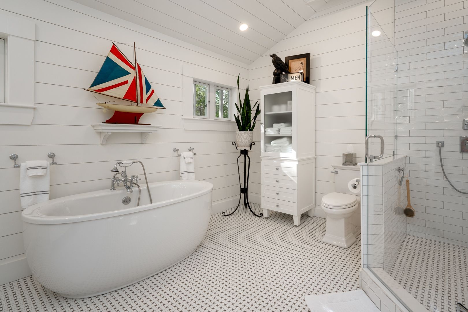 Bright white bathroom with freestanding tub, glass shower, hex tile floor, and nautical wall art.