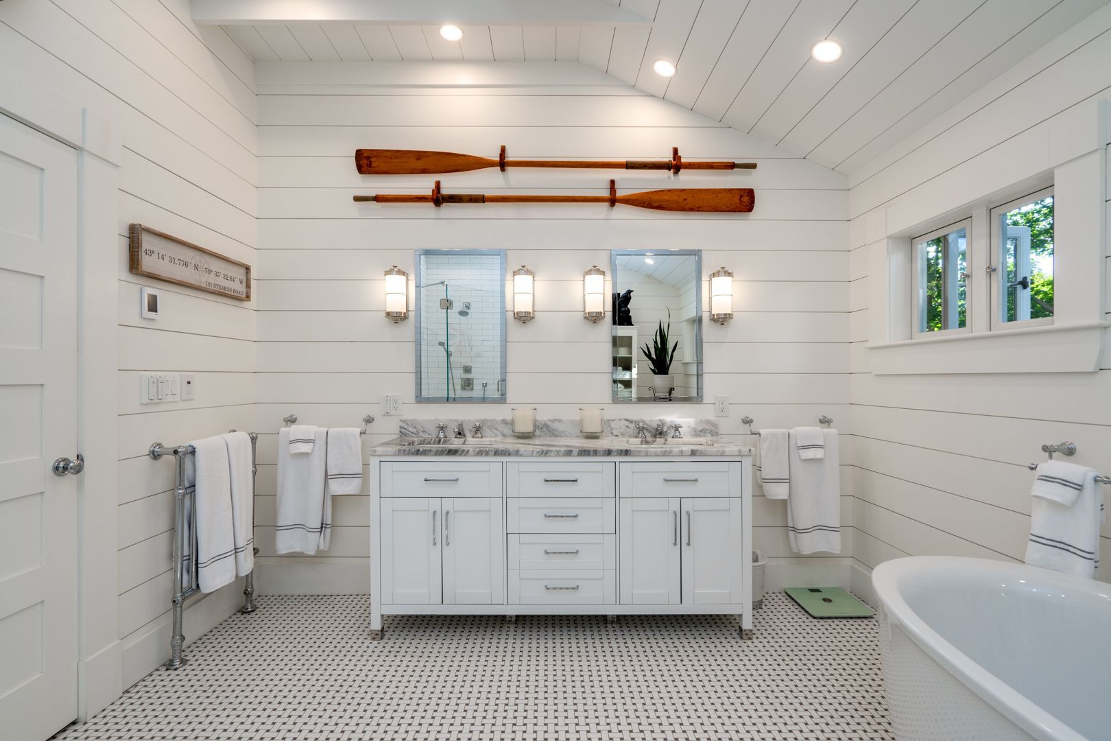 Bright white bathroom with double vanity, mirrors, wall sconces, and freestanding tub