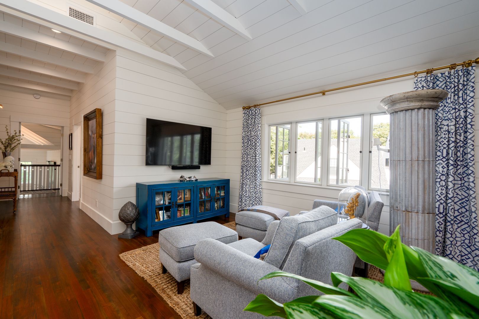 Bright living room with blue sofa, wall-mounted TV, hardwood floors, and large window with patterned curtains
