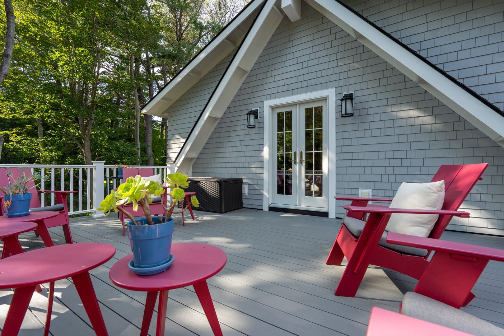 Pink patio chairs and potted flowers on a gray deck outside a cottage with French doors
